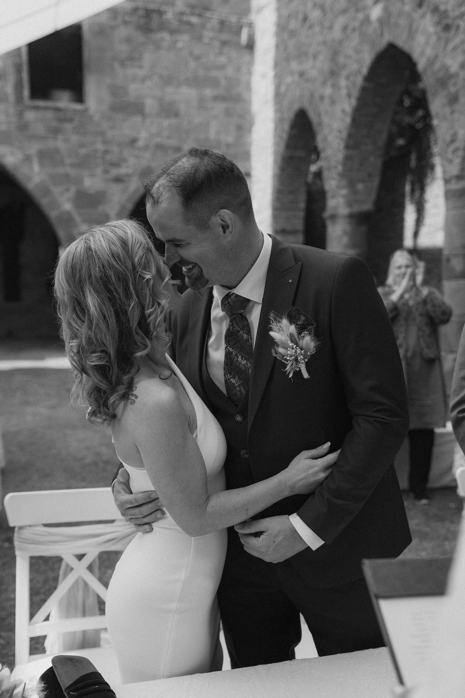 A romantic black and white wedding moment captured in an elegant stone archway setting.