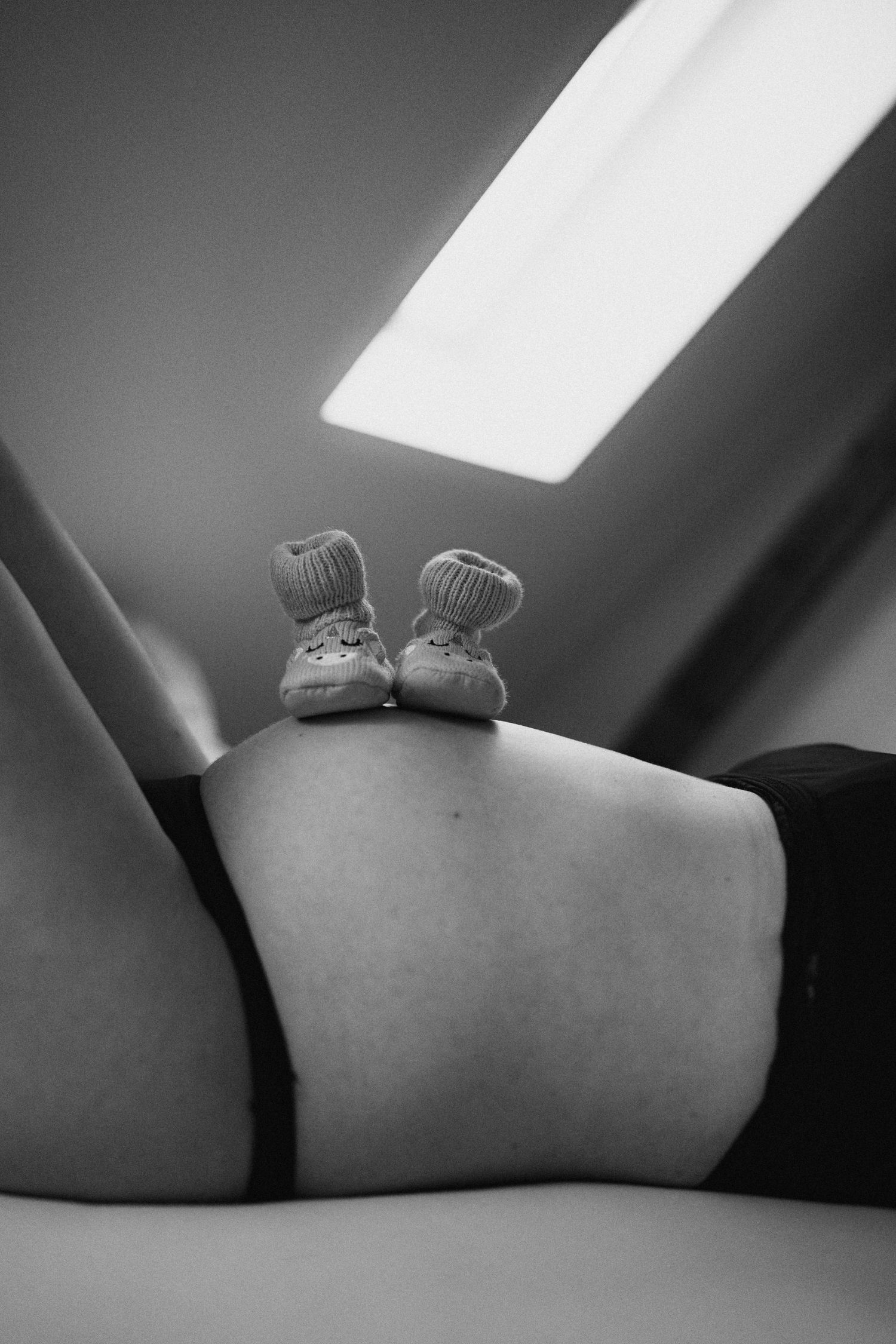 Black and white artistic photo series of a pregnant belly with baby shoes.
