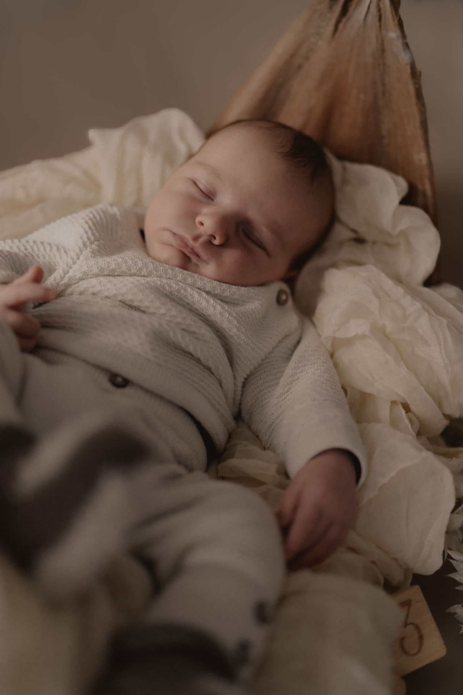 Peaceful newborn baby sleeping in a cozy basket, dressed in a soft white knit outfit with delicate buttons.