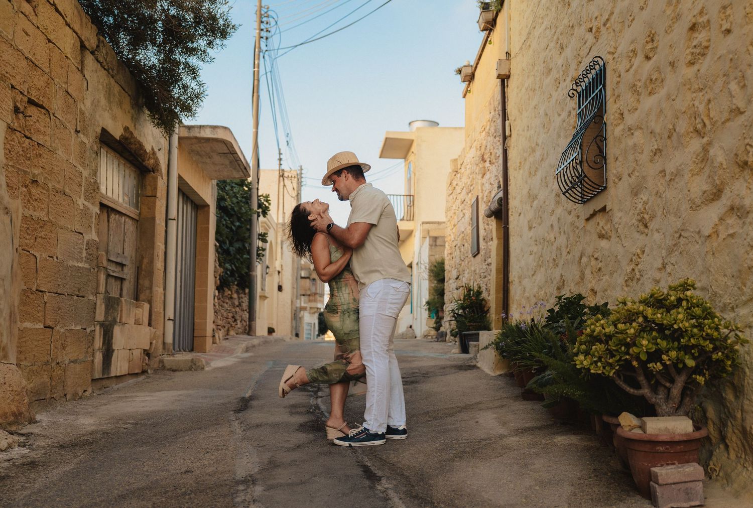 Couple sharing a romantic embrace on a narrow stone alley in a Mediterranean village at golden hour.
