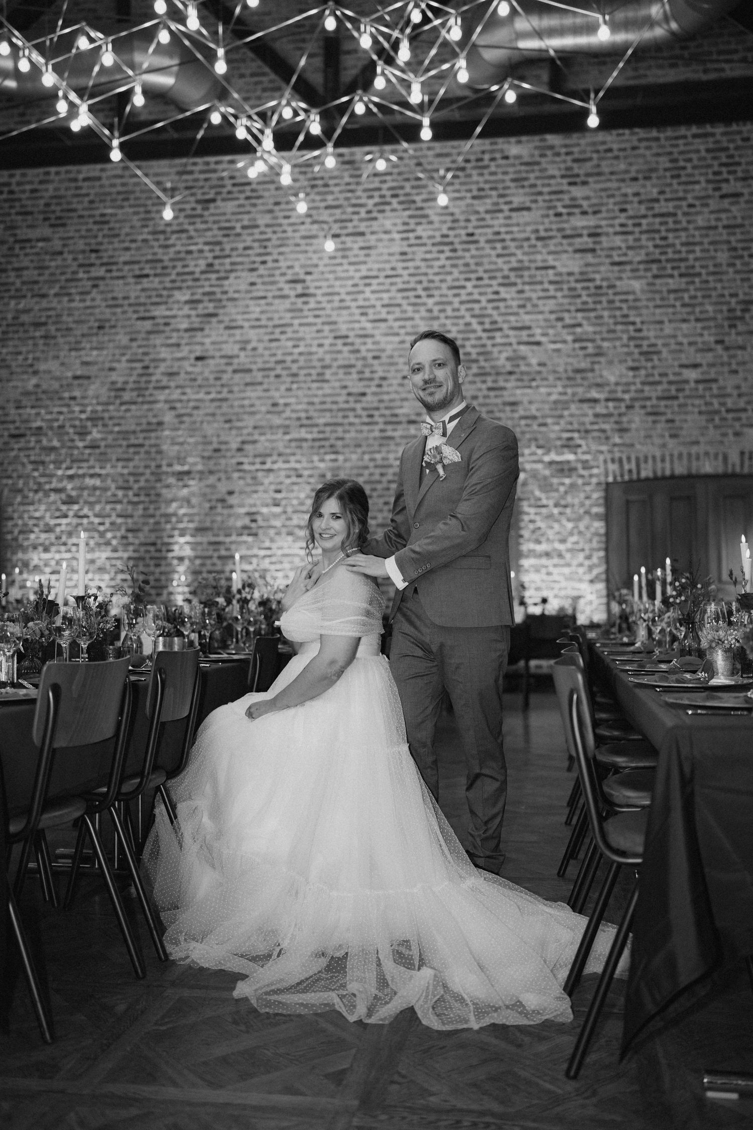 Black and white wedding photo series showing couple dancing in elegant venue with brick walls and string lights.