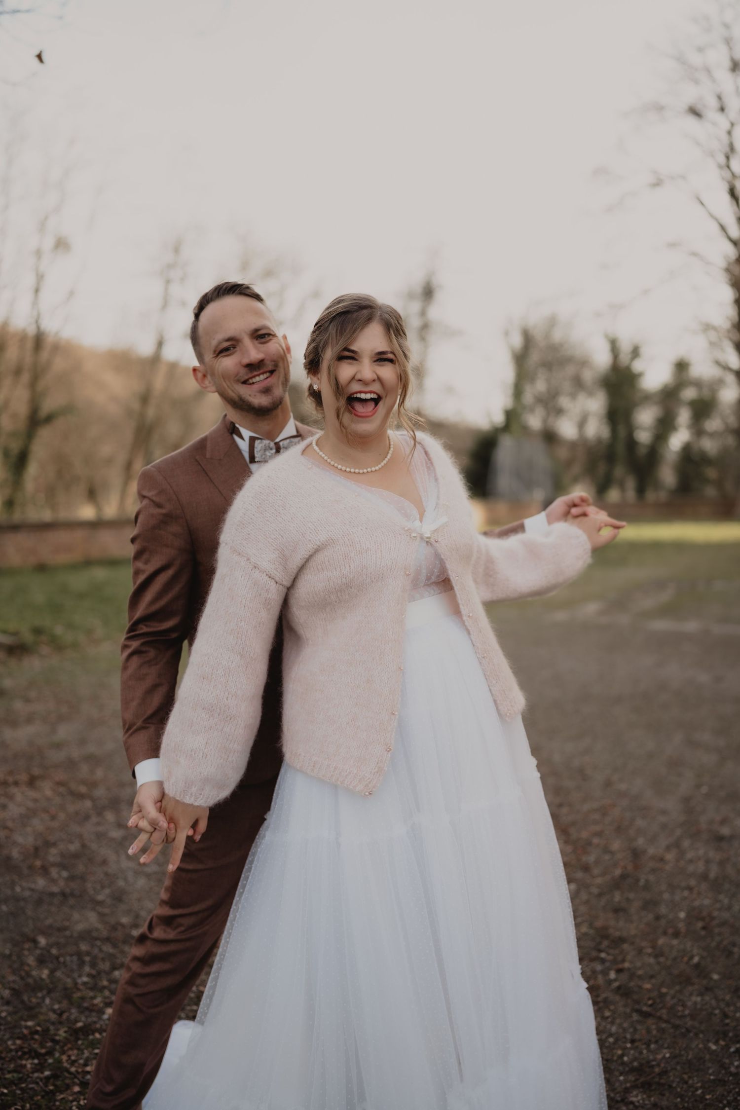 Joyful wedding couple laughs together during outdoor photo session in winter landscape.