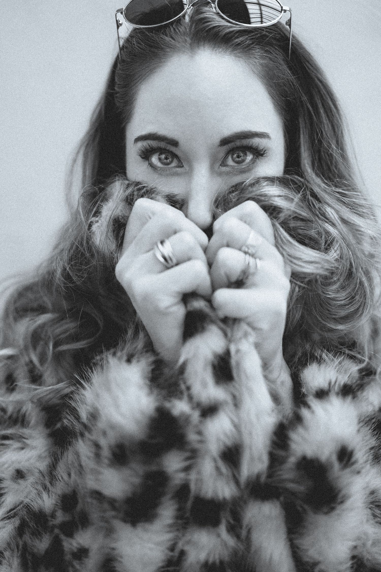 Black and white portrait of woman hiding face in leopard fur coat with sunglasses on head.