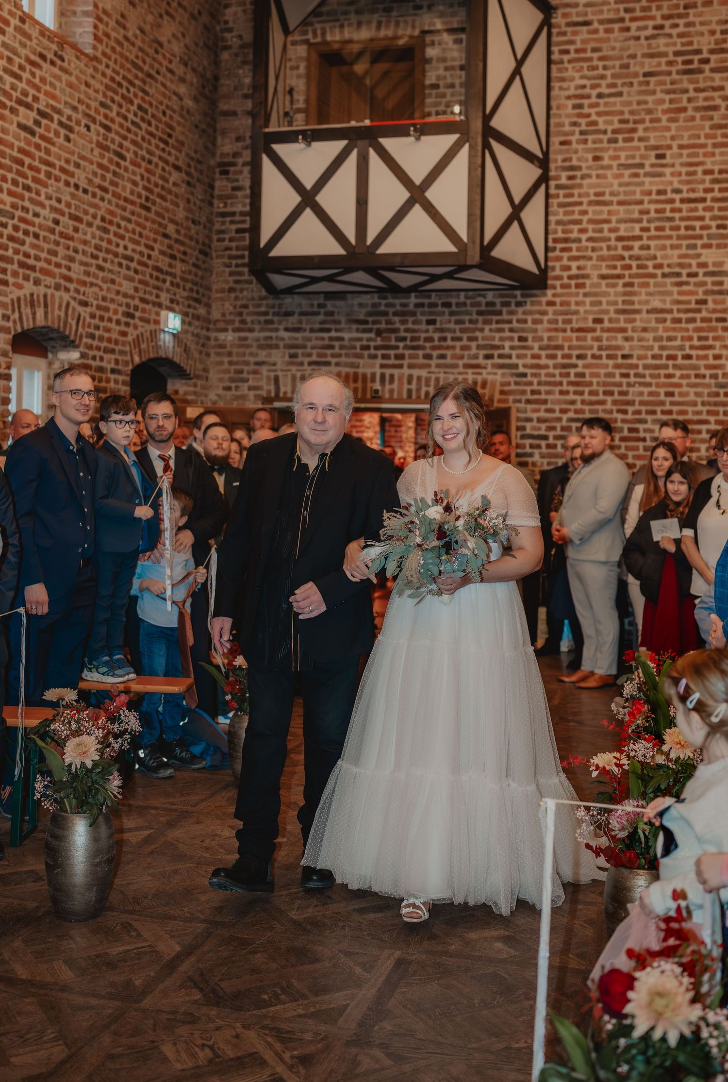 Wedding reception gathering in a rustic brick venue with exposed beams and decorative floral arrangements.