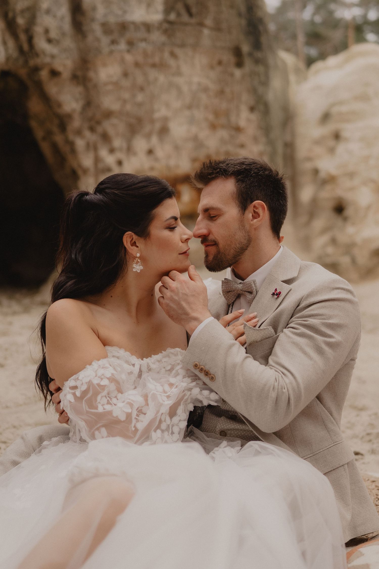 Romantic wedding couple shares intimate moments in a rustic stone setting wearing beige and white attire.