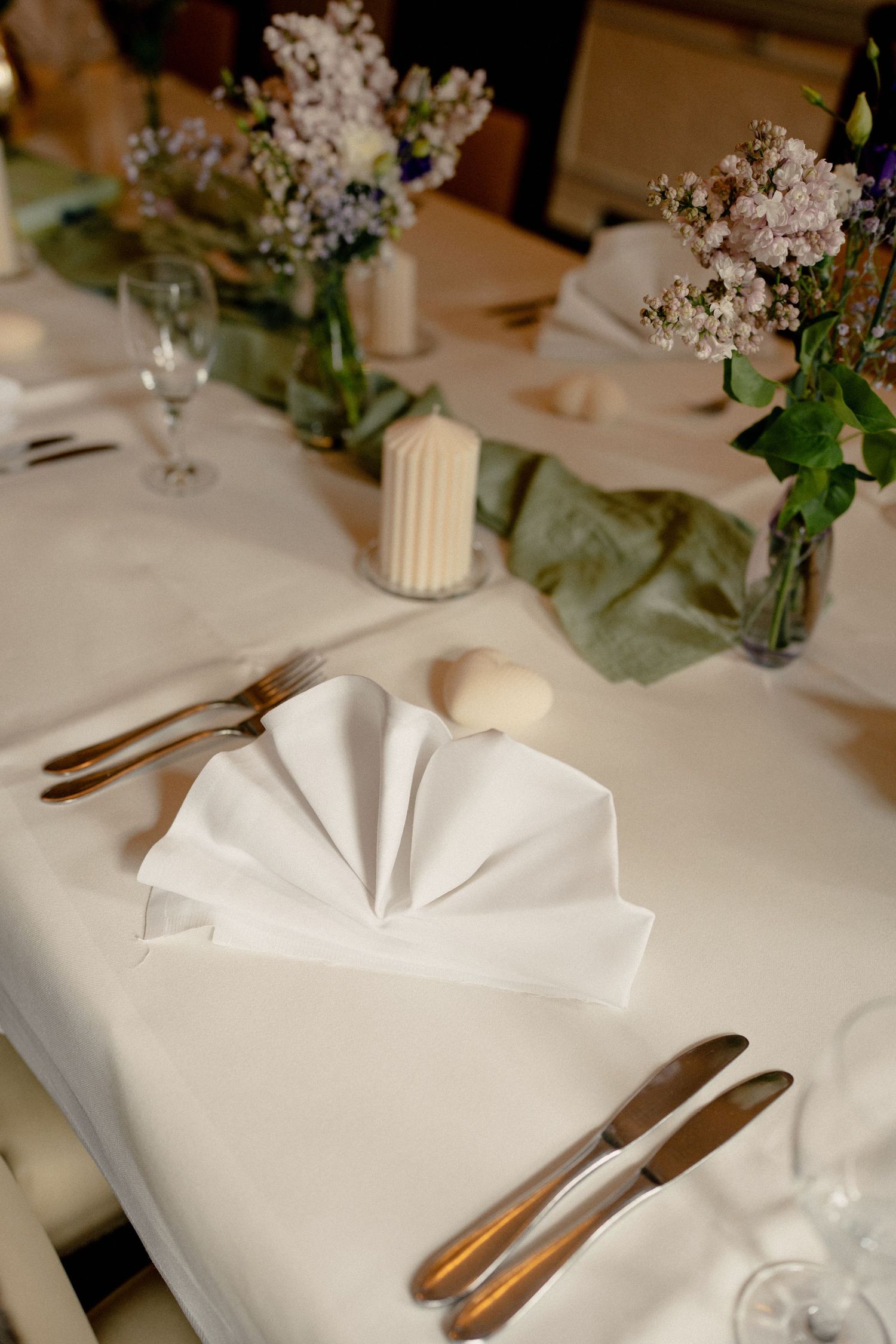 Elegant wedding table setting with white napkins, gold cutlery, candles, and floral centerpieces.