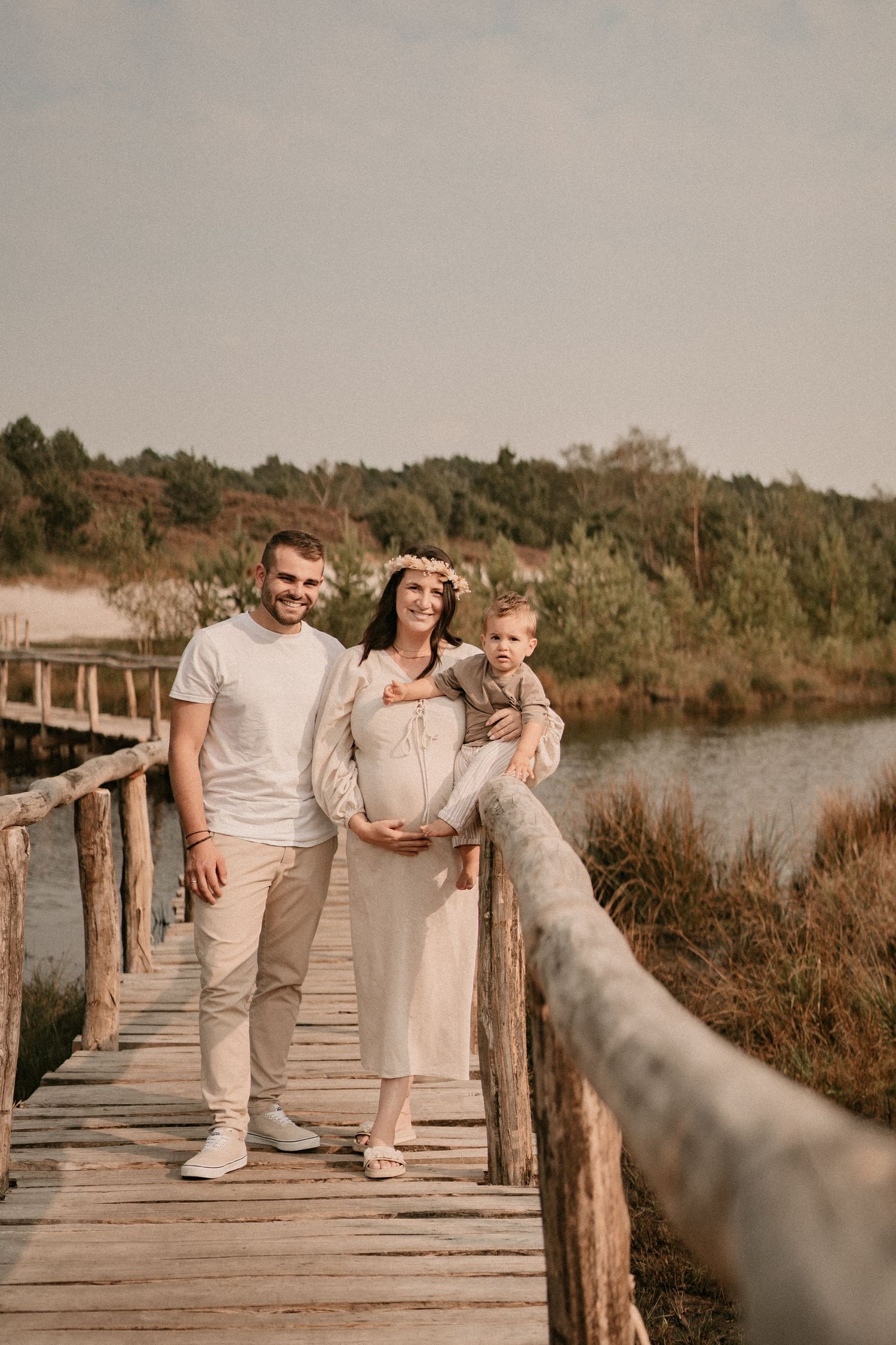 A family poses on a wooden boardwalk during a maternity photoshoot near a river.
