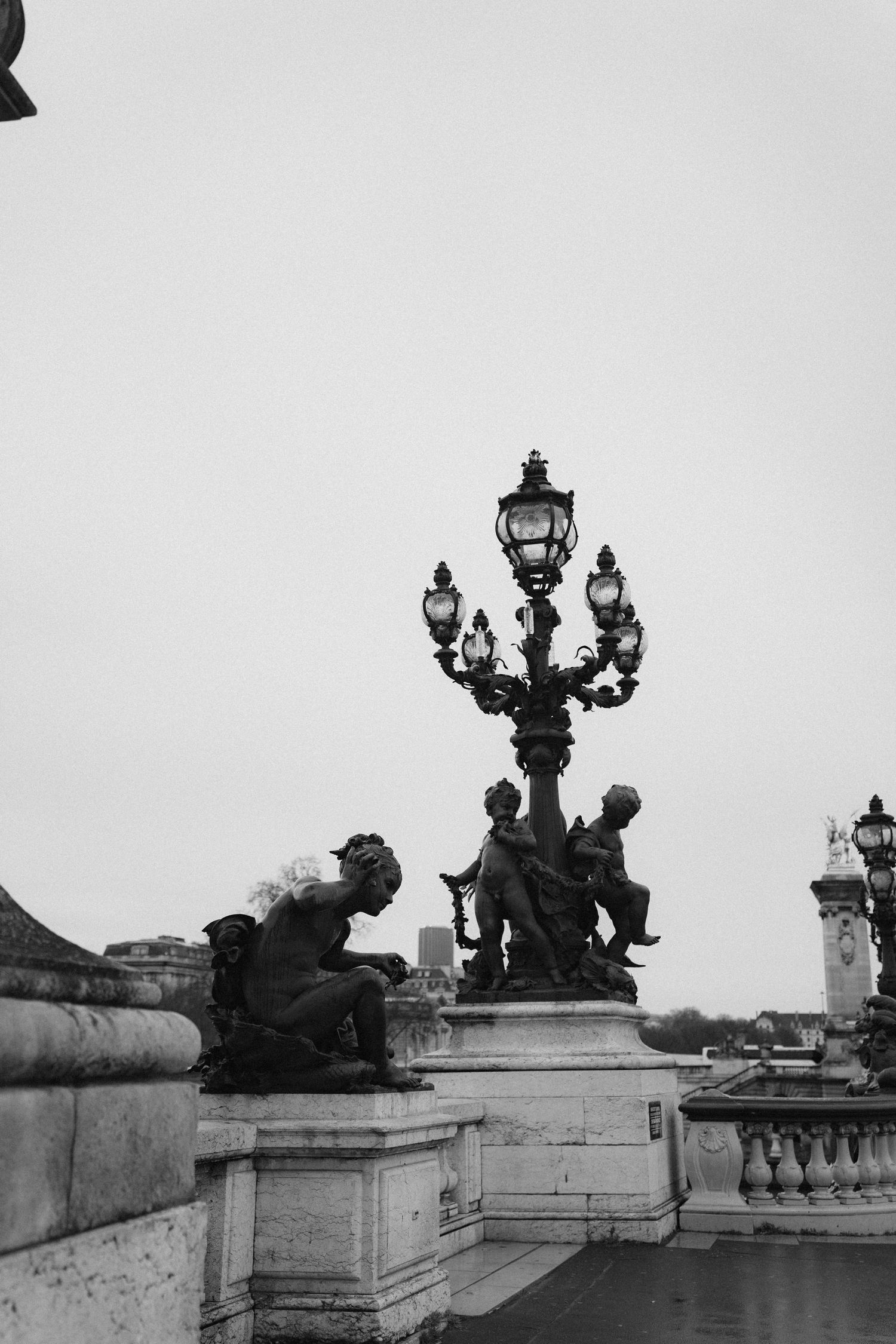 Black and white architectural detail of ornate Parisian bridge lampposts and sculptures.