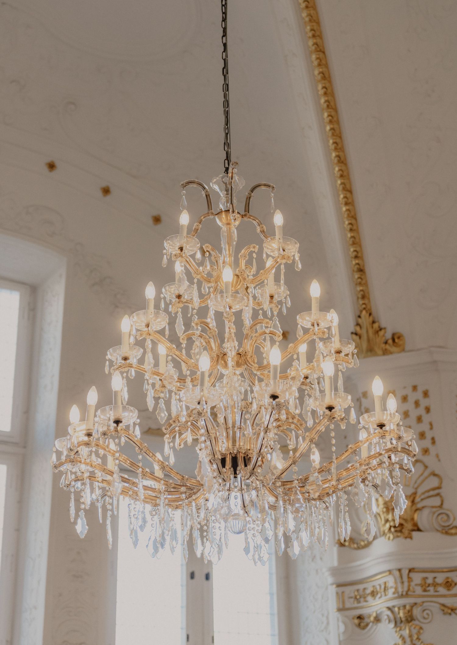 Crystal chandelier hanging in an ornate white and gold ballroom.
