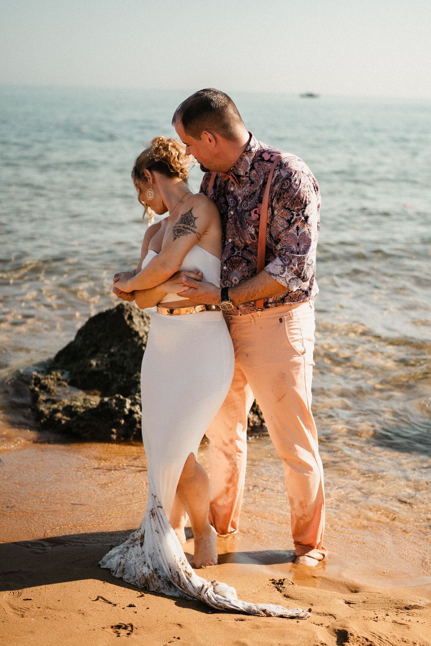 A tender moment between newlyweds on a sandy beach with ocean waves in the background.