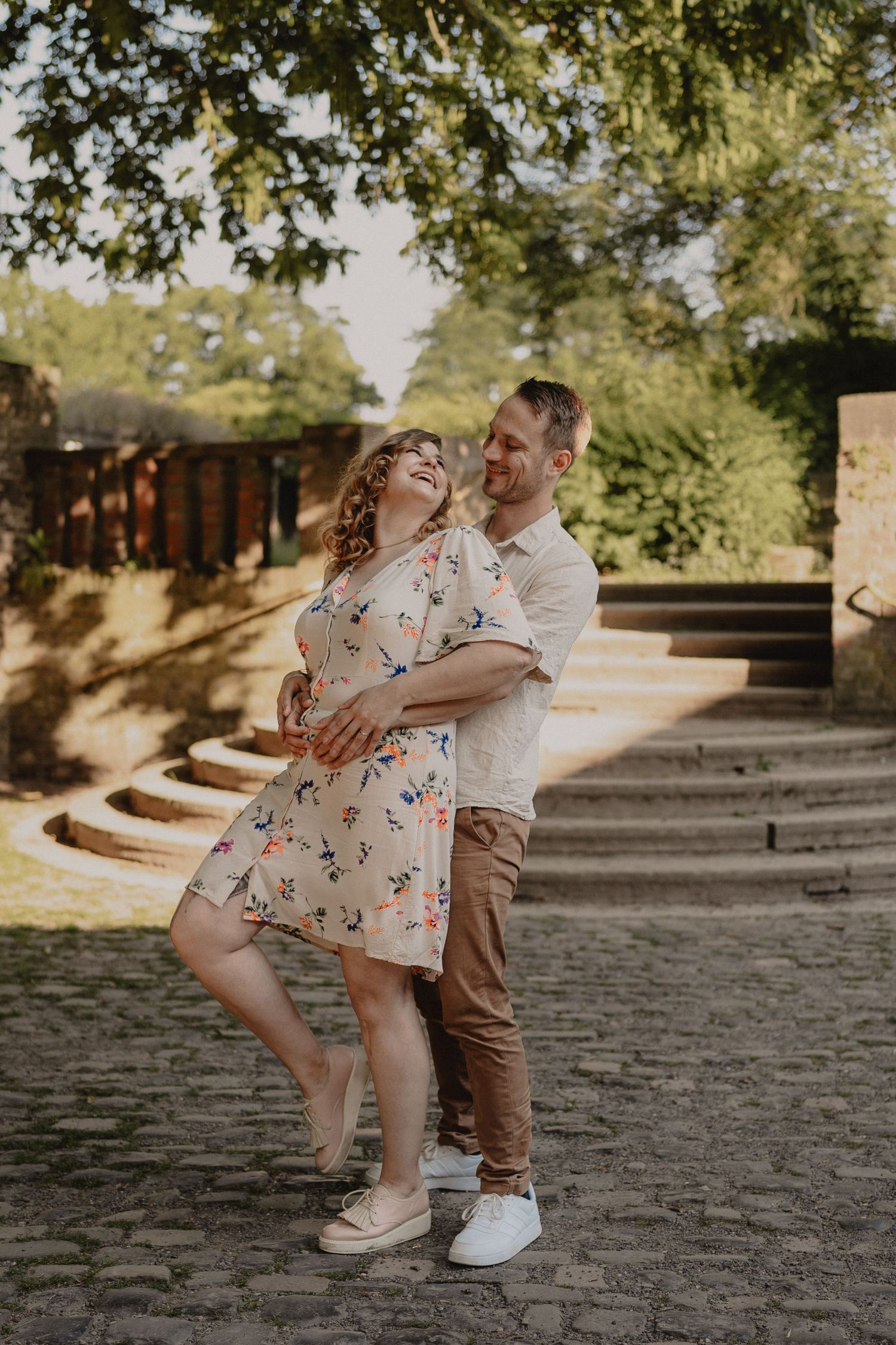 A couple dancing and laughing together on stone steps in a sunny garden setting.