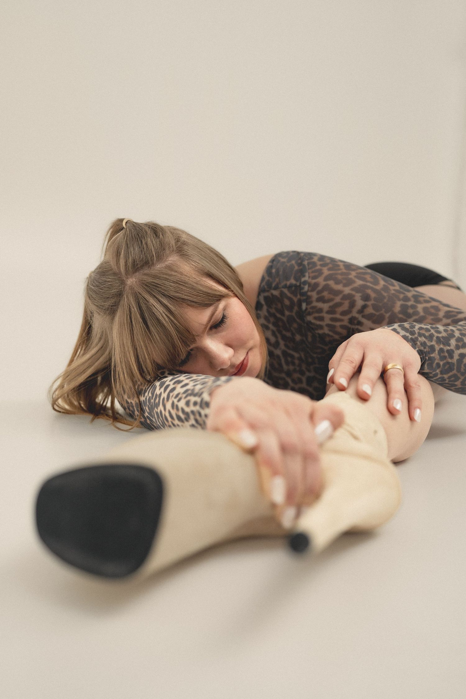 Woman in leopard print outfit lying on floor reaching toward a cream high heel shoe.