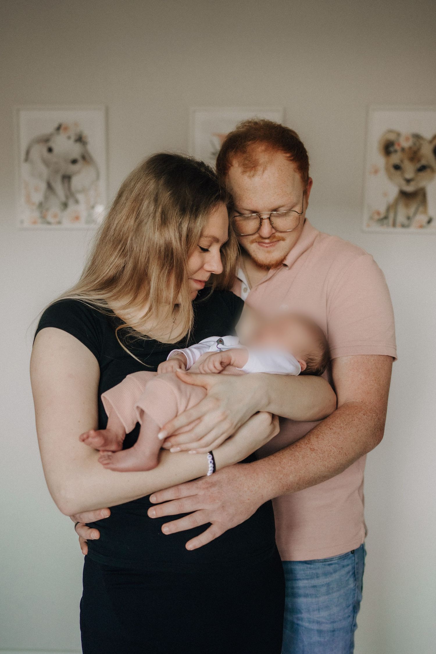 A tender family moment captured indoors with a newborn baby, with animal artwork visible on the wall behind them.