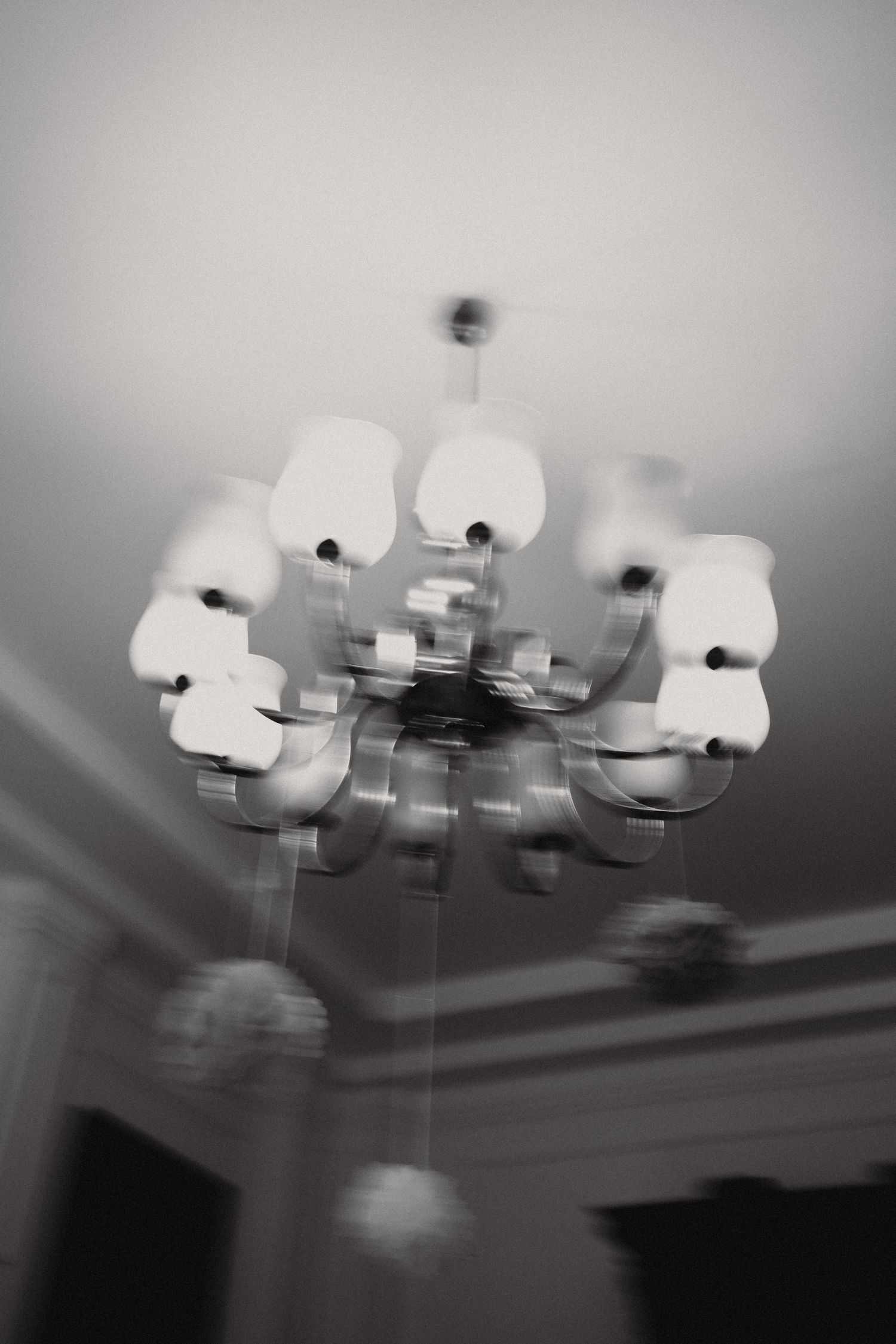 Blurry black and white photo of a modern chandelier with globe lights hanging from a ceiling.