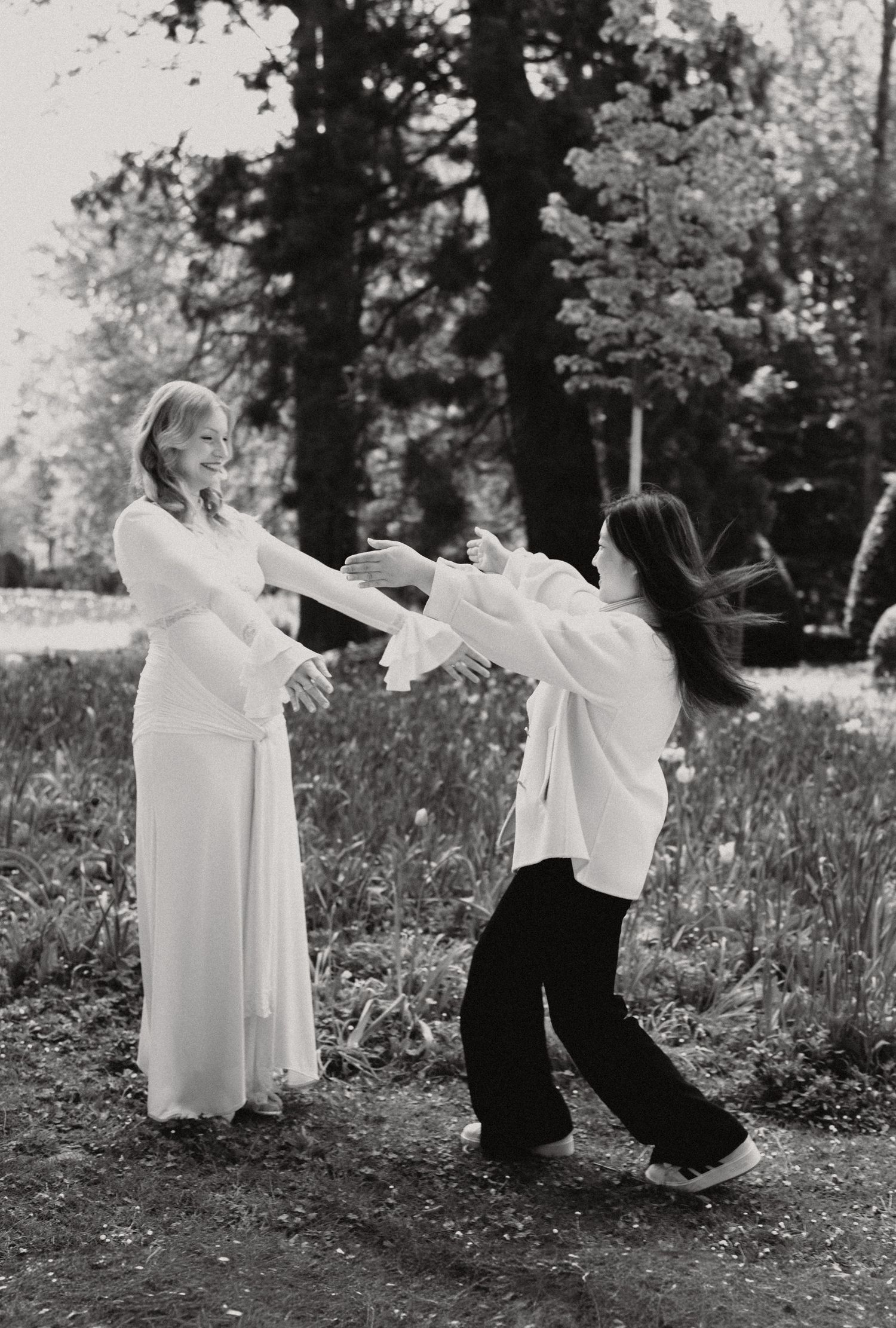 Black and white photo of two women playfully dancing together in a sunlit garden park.