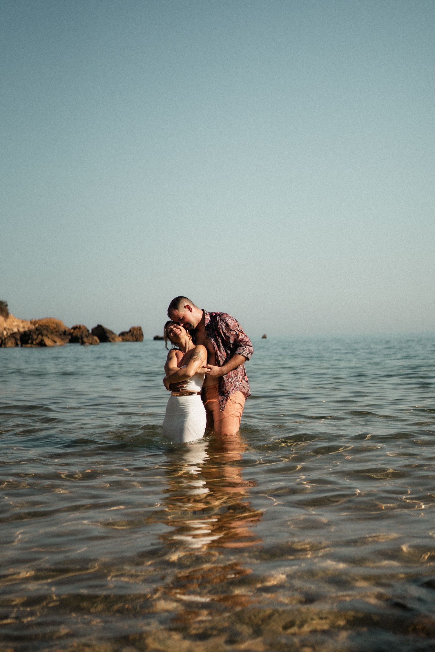 A couple shares an intimate moment while standing in shallow ocean water during sunset.
