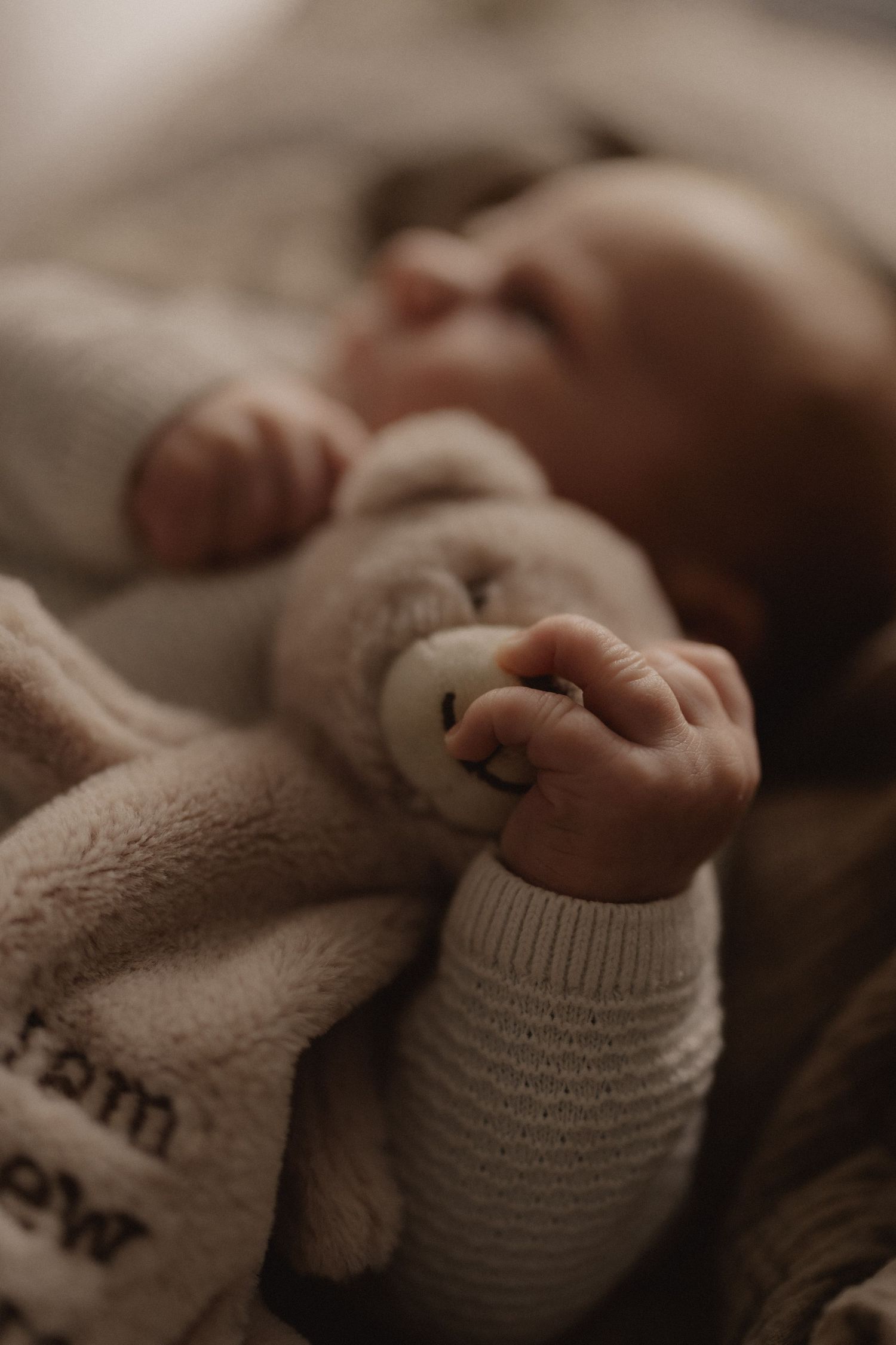 Close-up of tiny baby feet wearing white knitted socks against soft beige blanket.