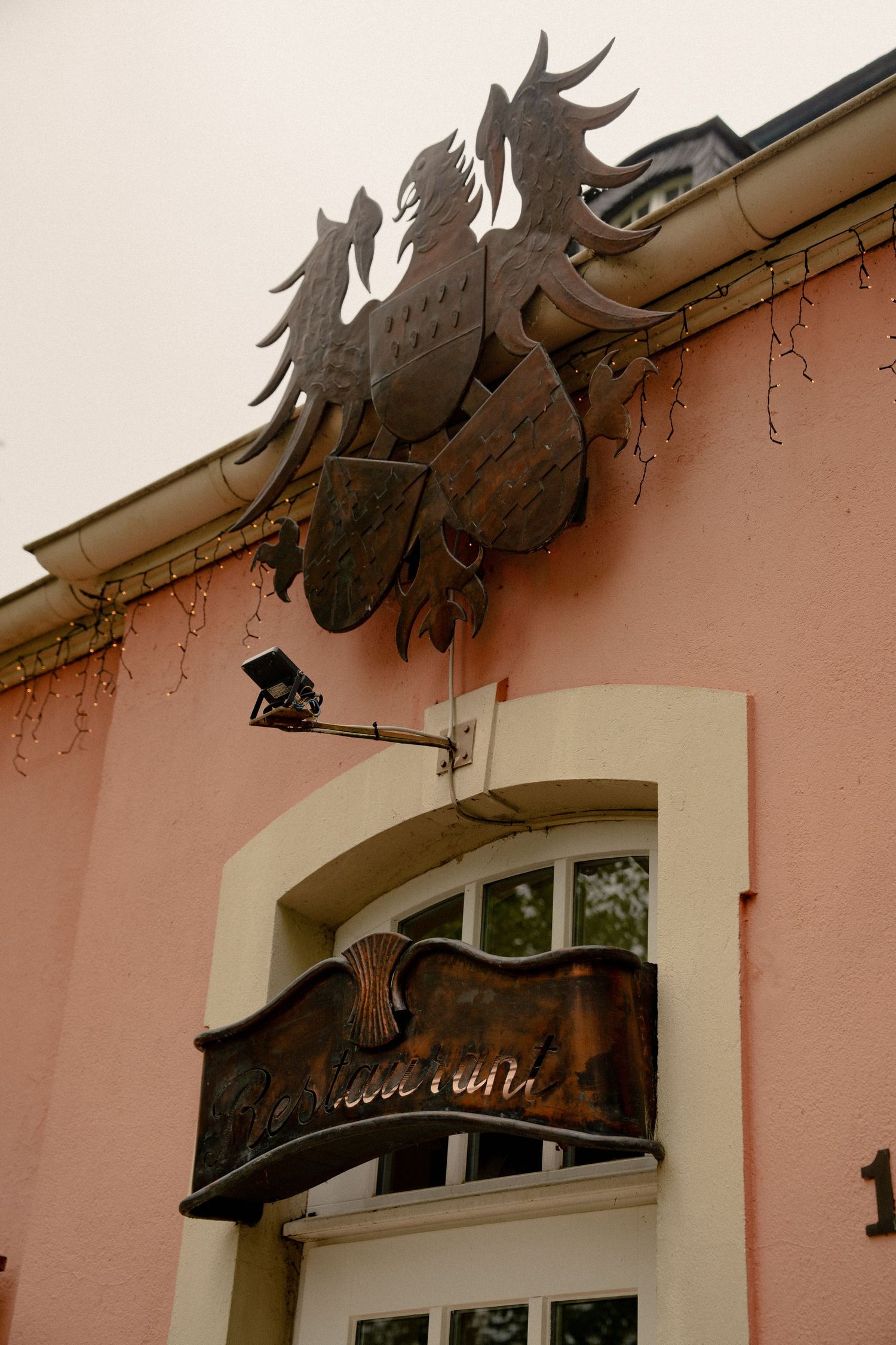 Ornate metal double-headed eagle coat of arms mounted on a pink building facade above an arched window with decorative signage.