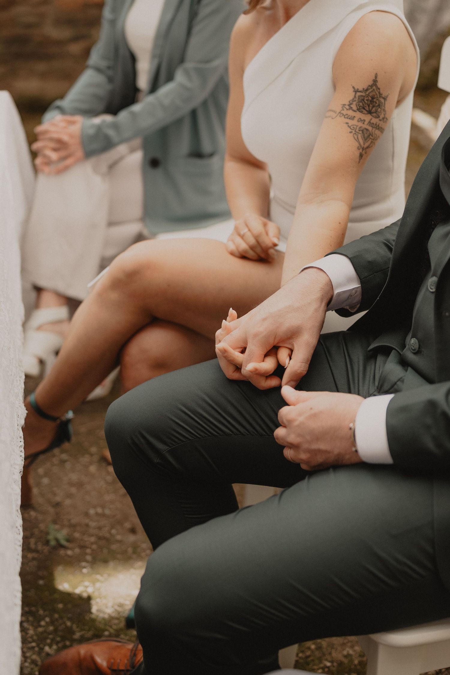 Close-up of couple holding hands during wedding ceremony with bride showing delicate arm tattoo.