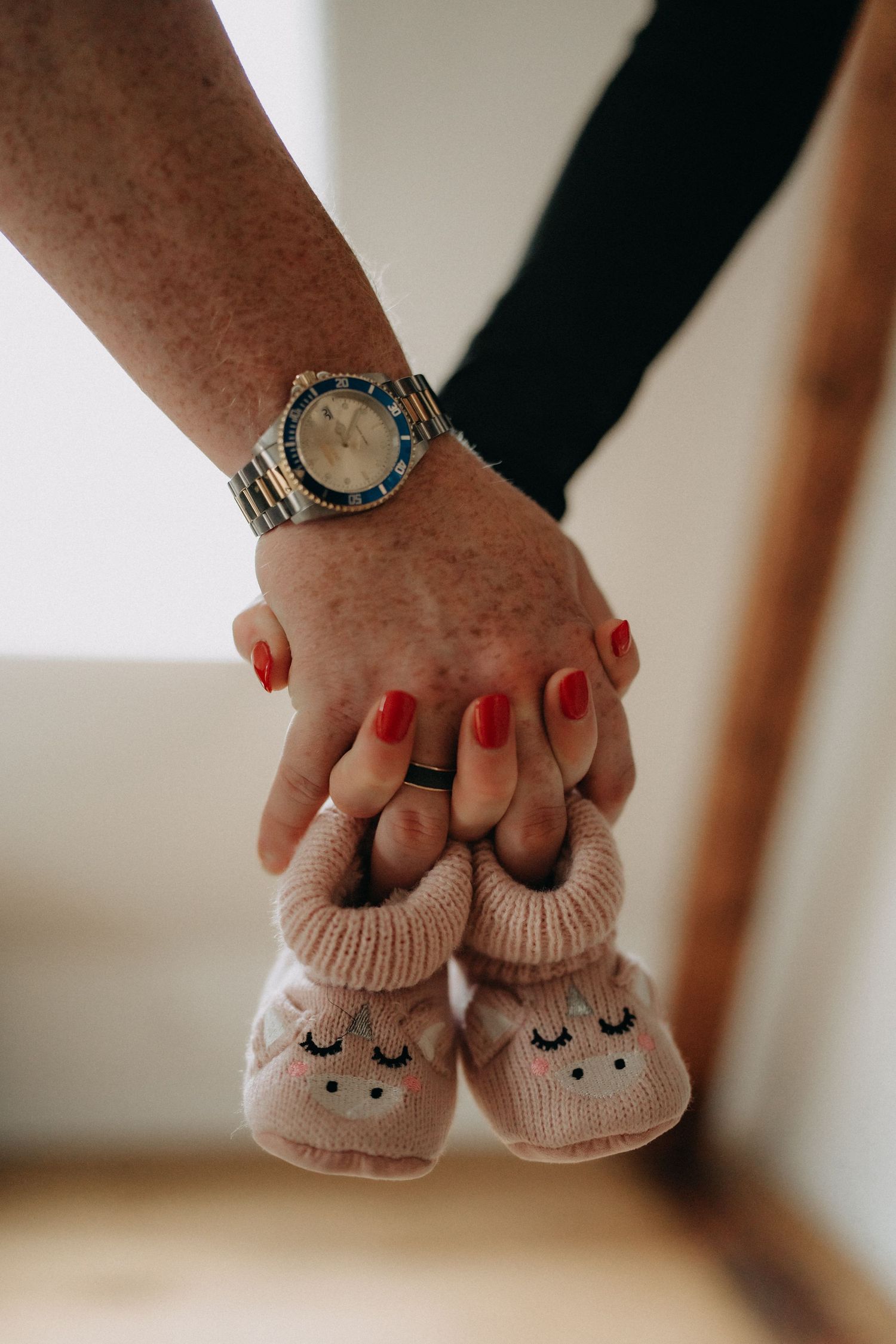 Tiny knitted baby booties held with a hand wearing red nail polish and a silver watch.