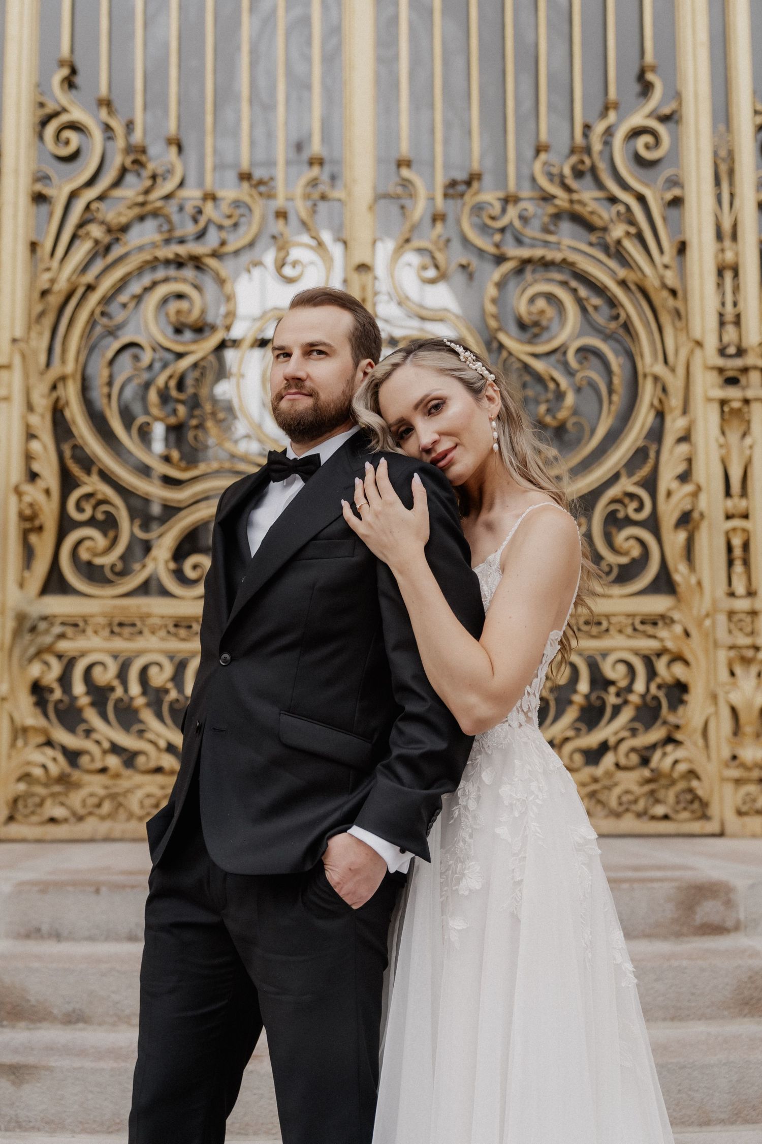 A romantic moment captured against ornate golden gates with elegant wedding attire.