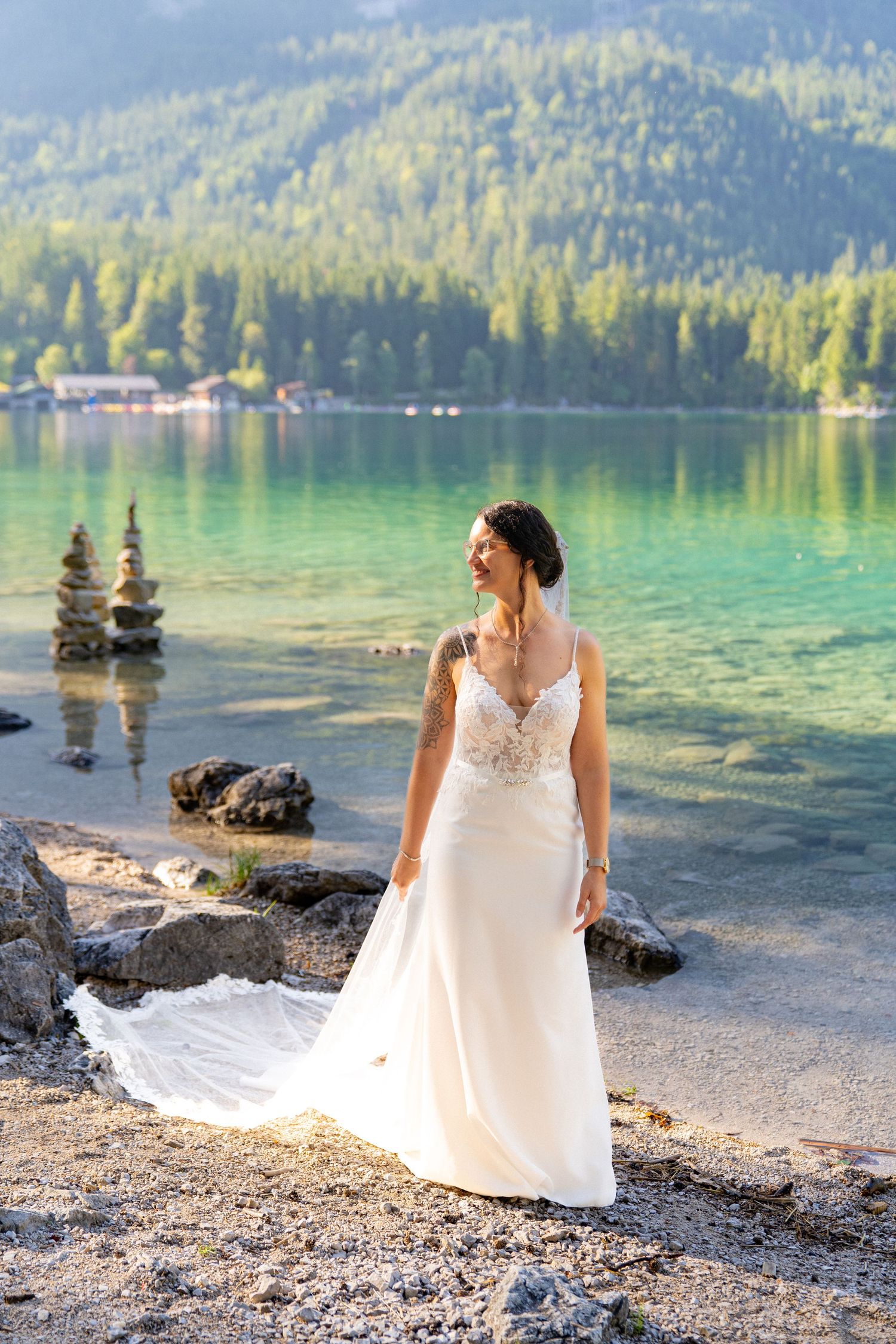 A white wedding dress flows elegantly along a rocky lakeshore with turquoise waters and mountain views in the background.