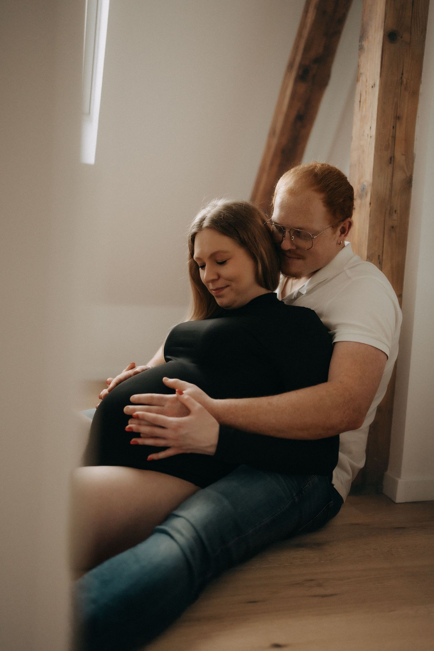 Intimate maternity photos showing couple embracing on wooden floor.