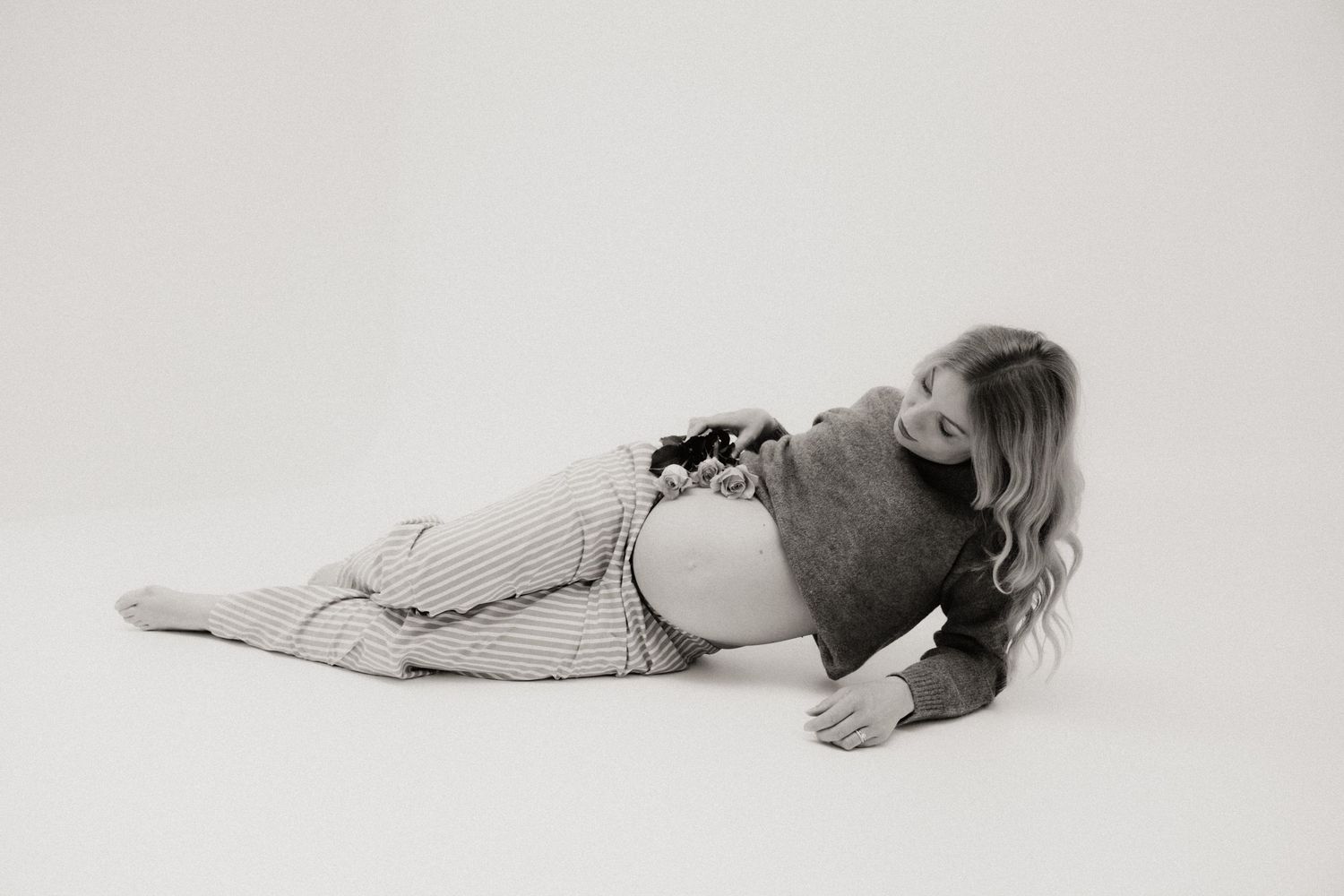 Black and white photo of a pregnant woman lying on her side in a striped outfit on a white background.