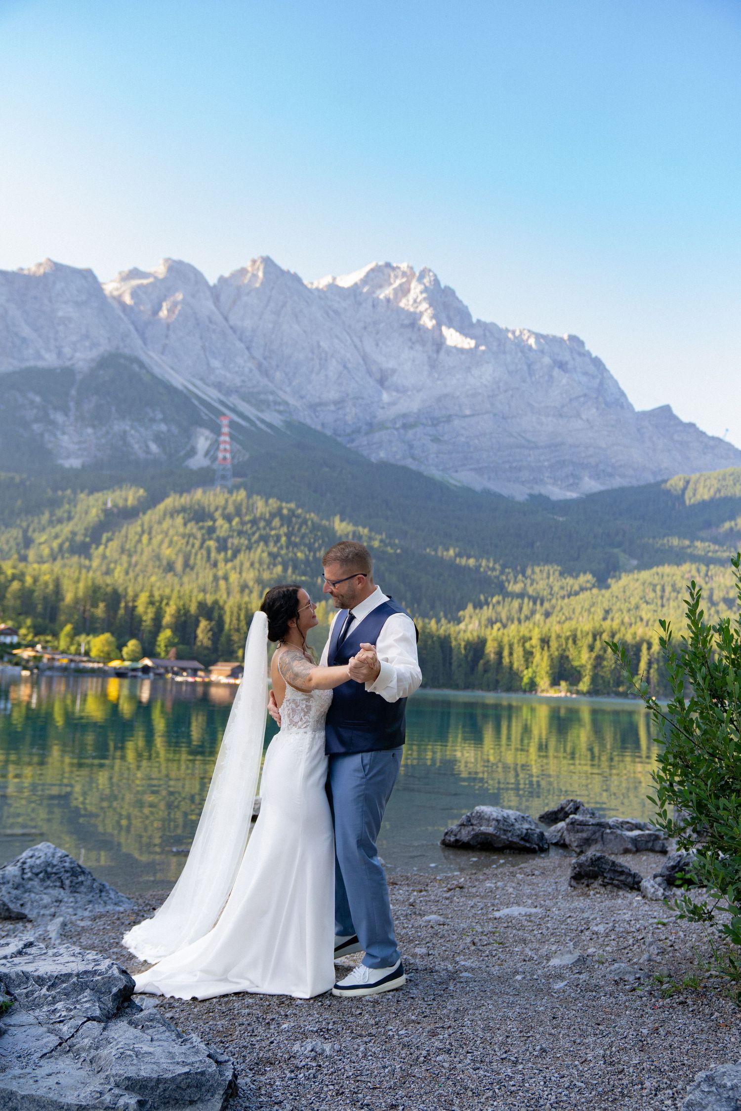 A couple shares an intimate moment by a scenic mountain lake with snow-capped peaks in the background.