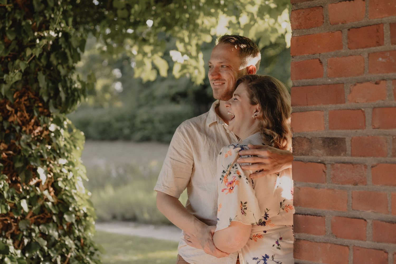Romantic couple sharing intimate moments against a brick wall with natural sunlight.