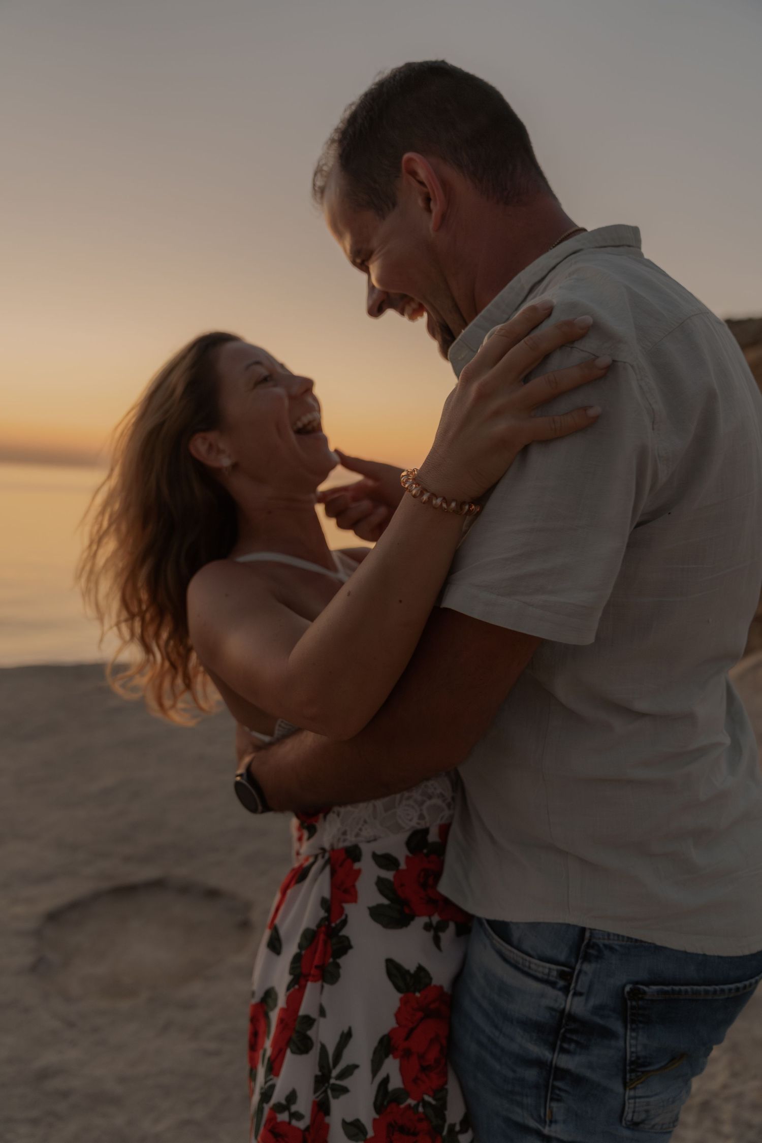 Romantic couple embracing on beach at sunset with warm golden light.