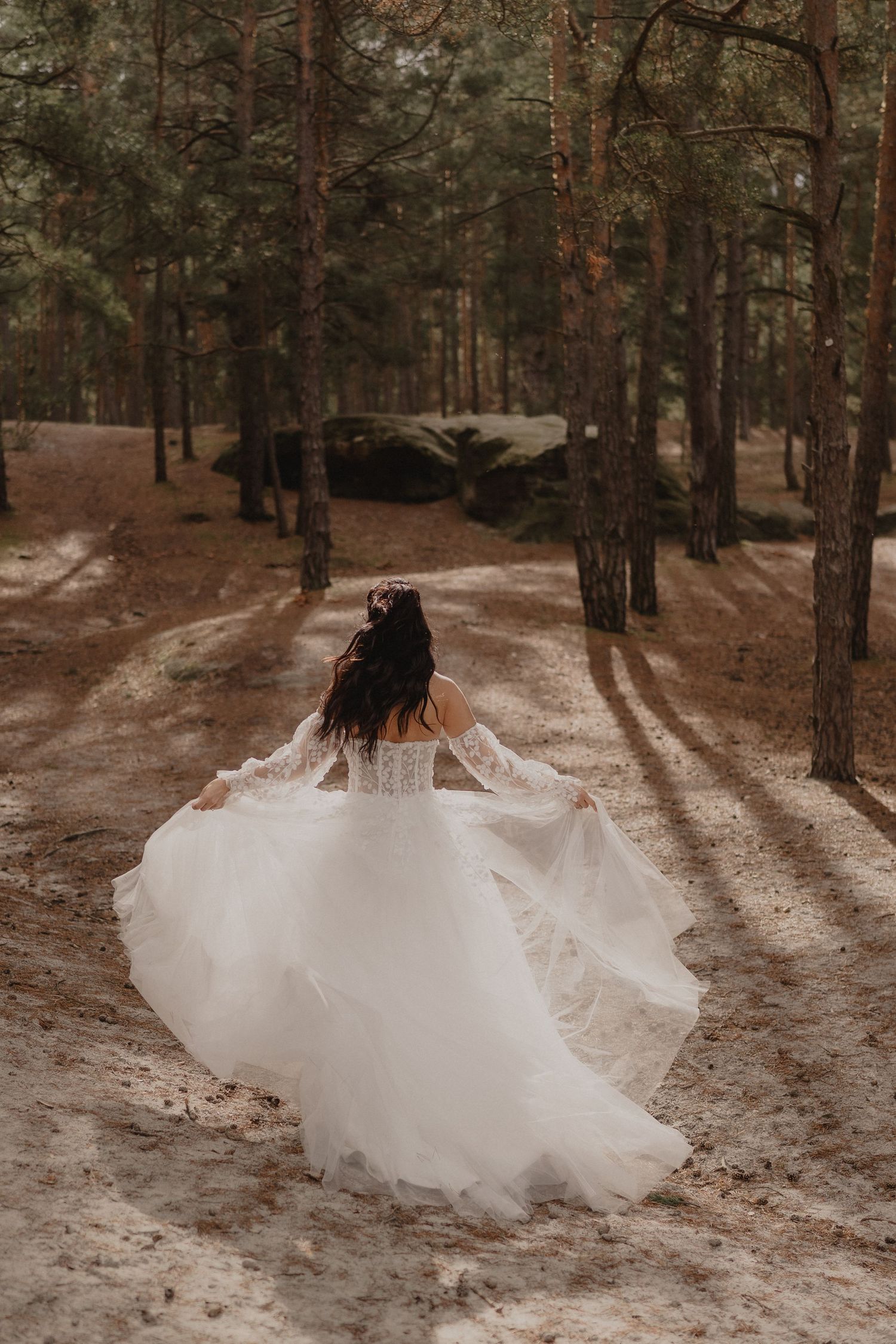 A flowing white wedding dress spins dramatically in a pine forest setting.