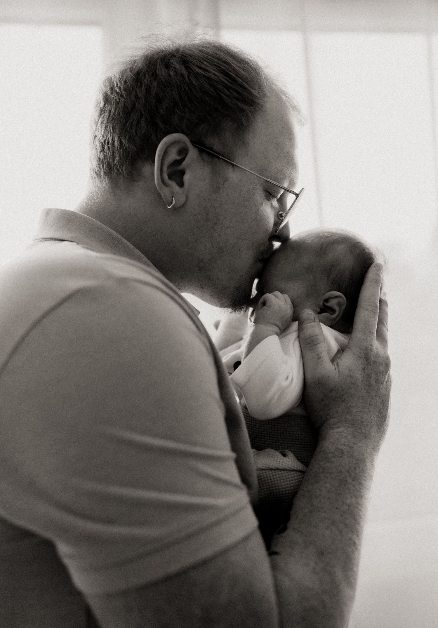 A series of black and white photographs showing someone holding and kissing a small baby in progressive frames.