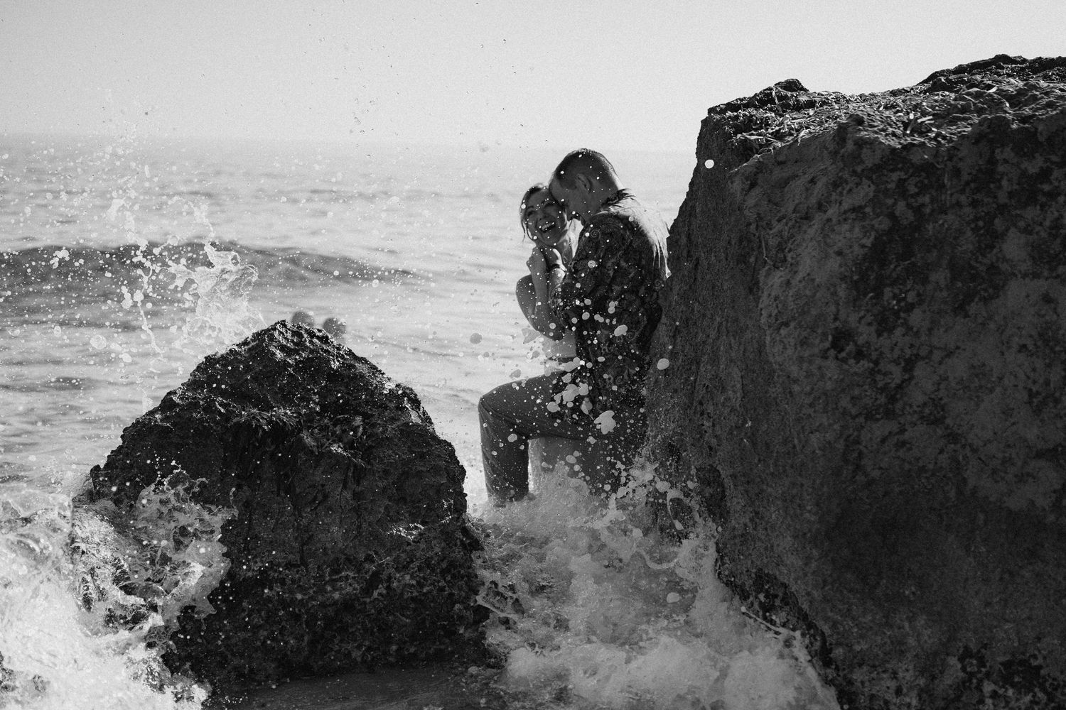 Dramatic black and white photo of waves crashing against coastal rocks at the beach.