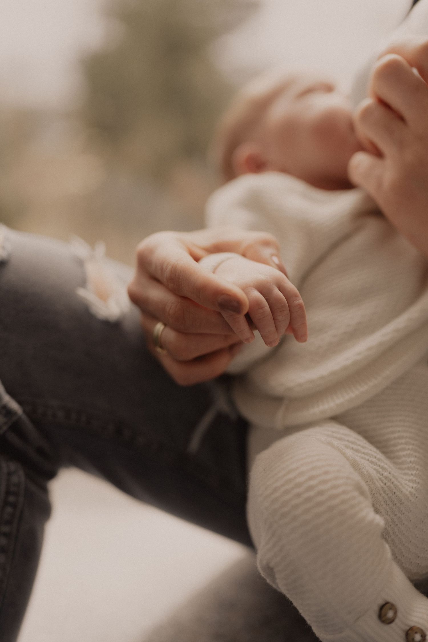 Detail shot of tiny baby hands against a cream knit sweater in soft lighting.