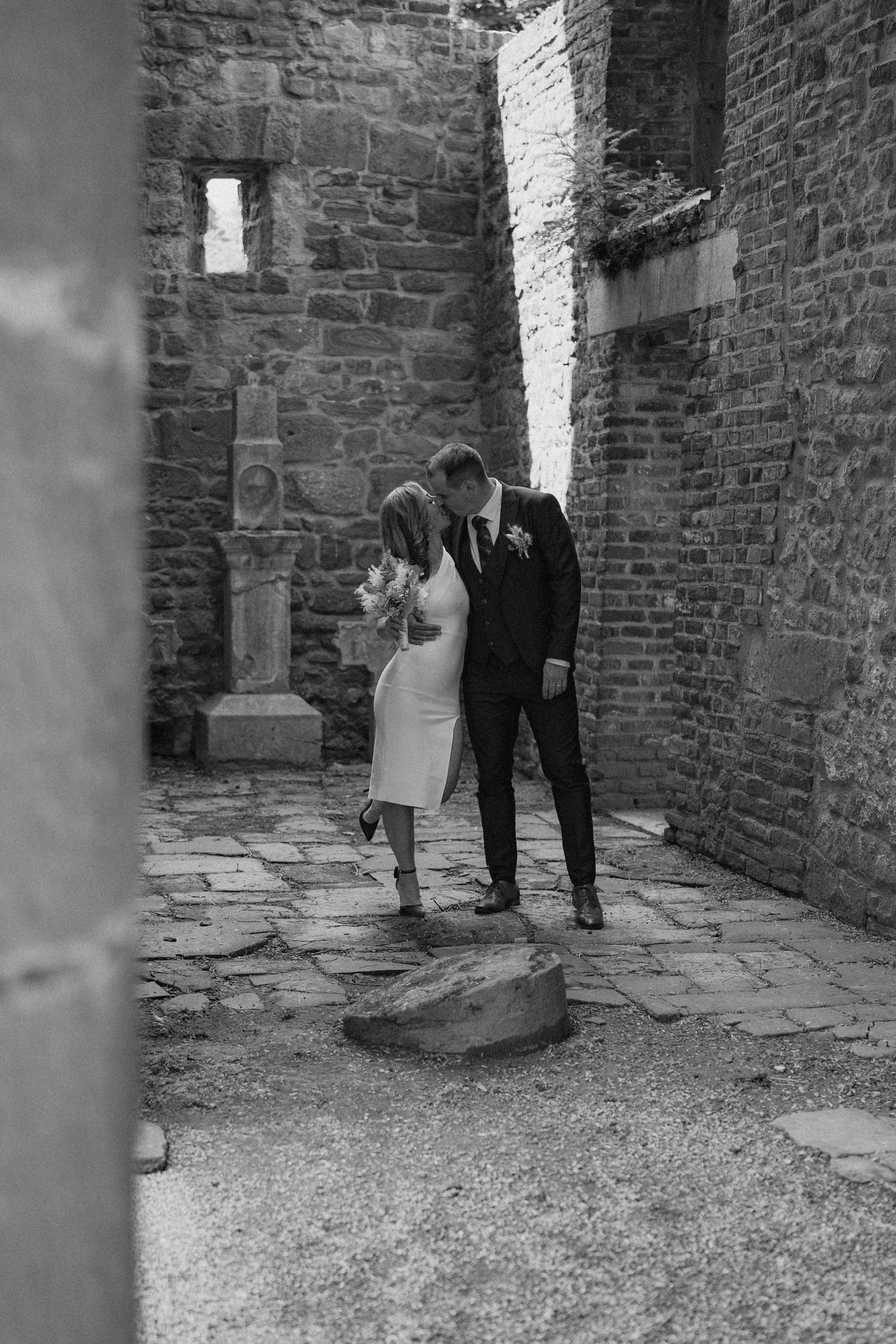 Black and white wedding photos capture tender moments between newlyweds against historic stone architecture.
