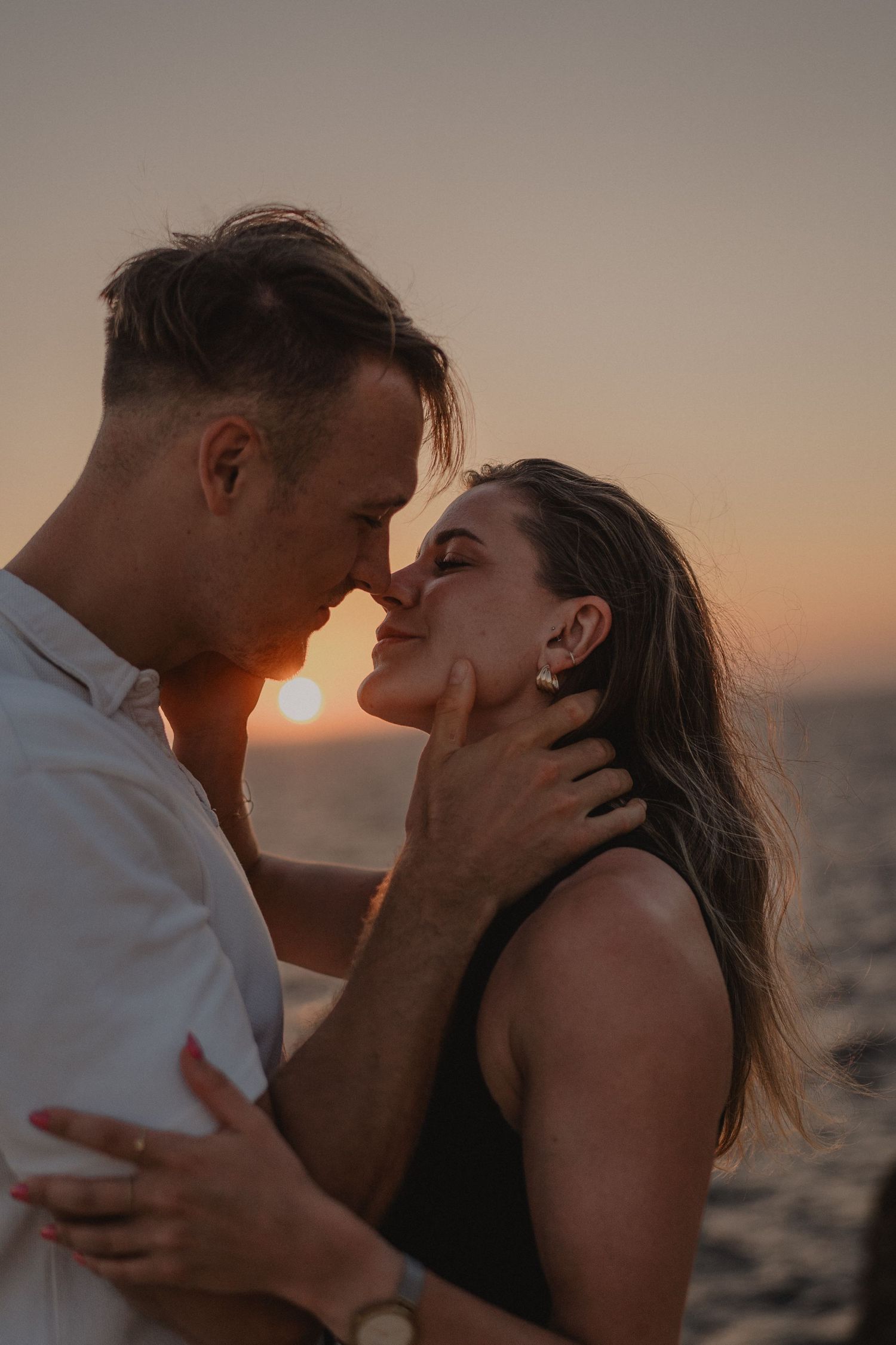 Romantic couple sharing an intimate moment at sunset by the ocean, man gently holding woman's face.
