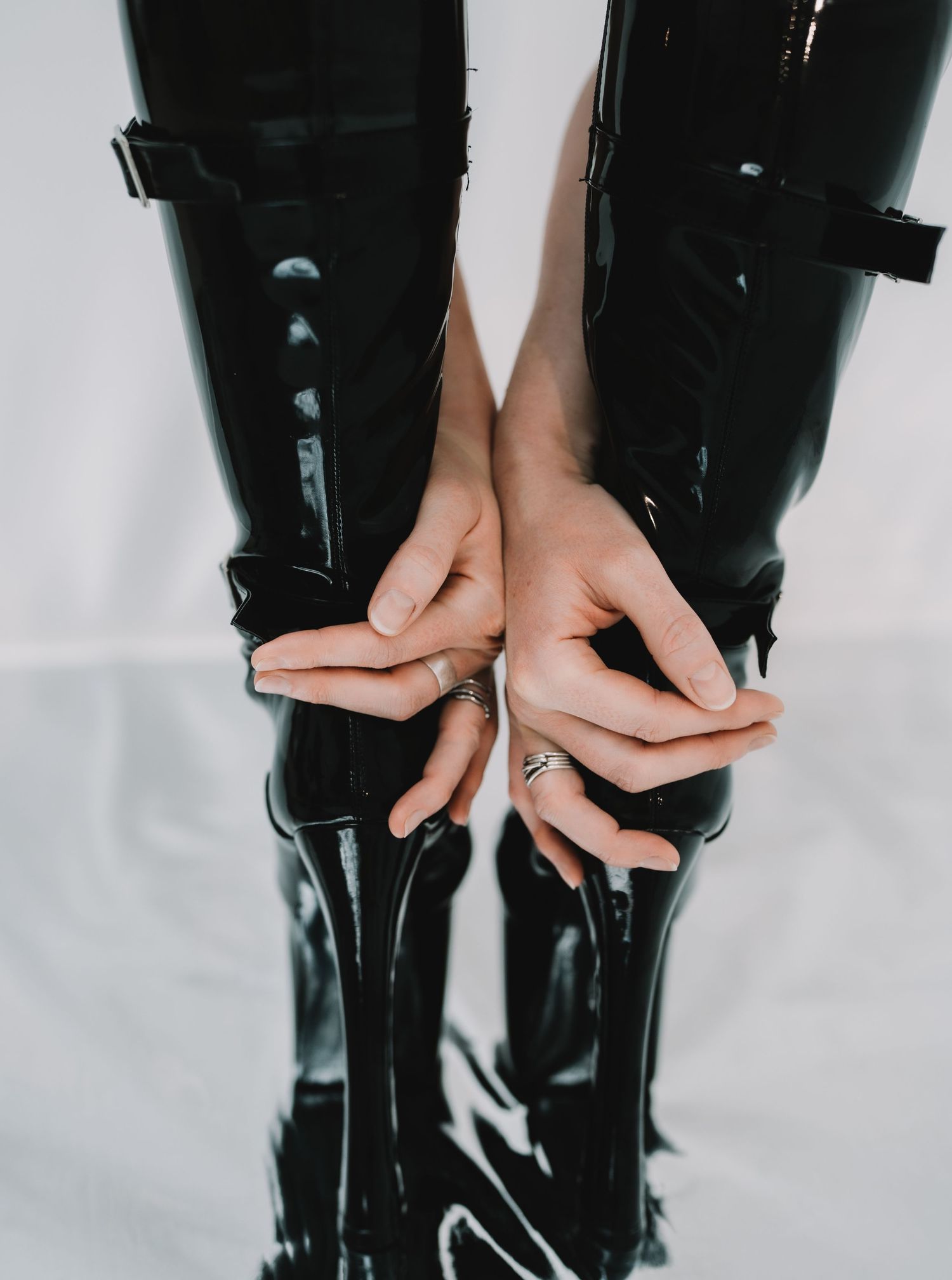 Hands unzipping a tall black patent leather boot in a sequence of progressive stages against a white background.