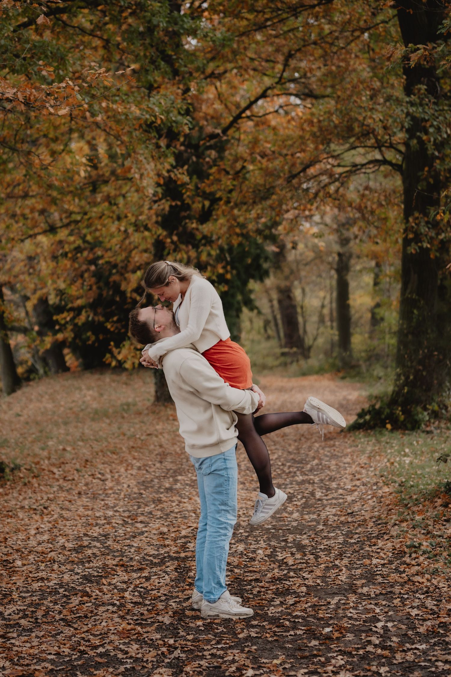 A playful lift pose captured during an autumn photoshoot with fallen leaves.