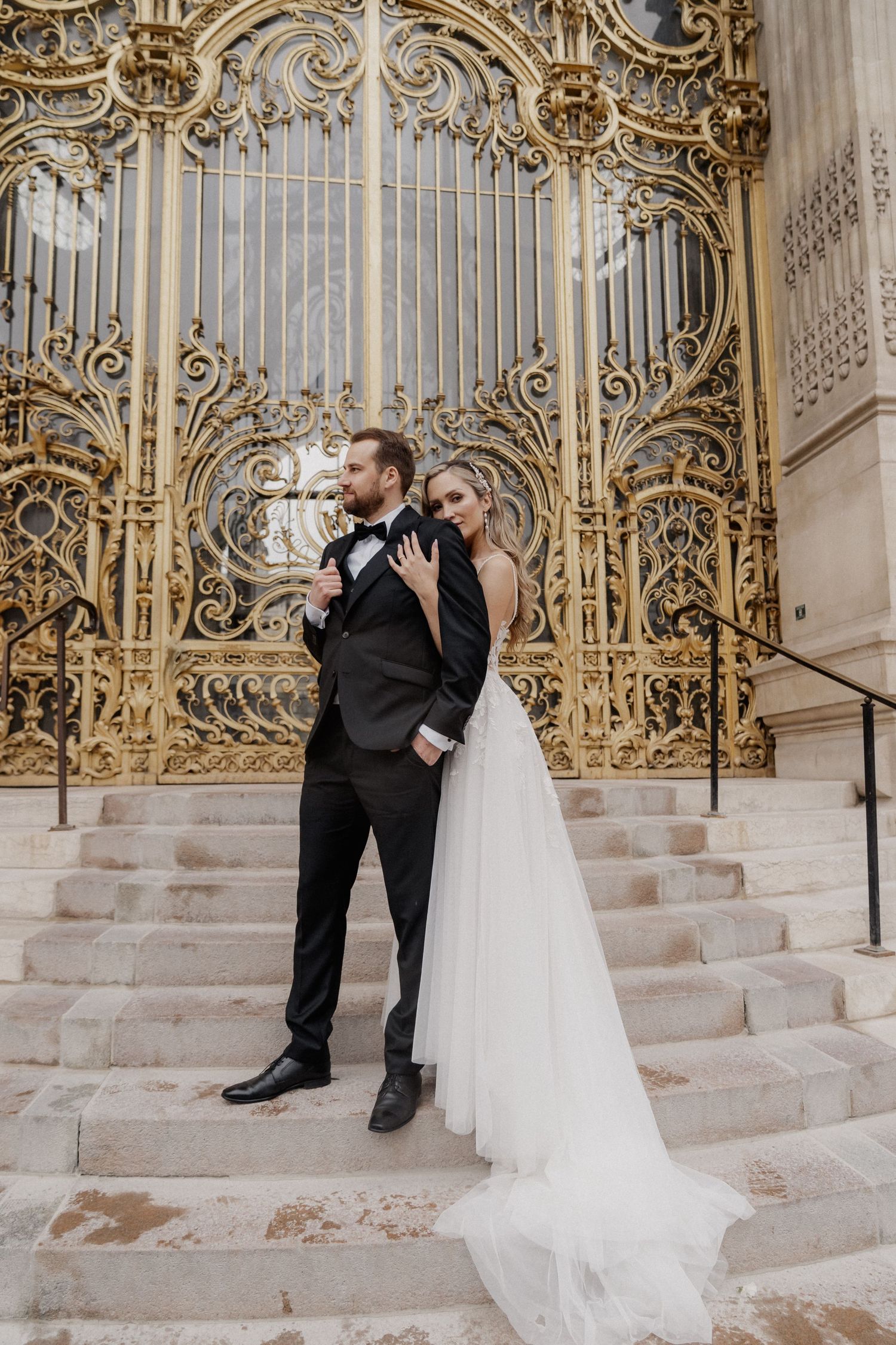 Wedding couple shares intimate moments on stone steps with ornate golden gates backdrop.