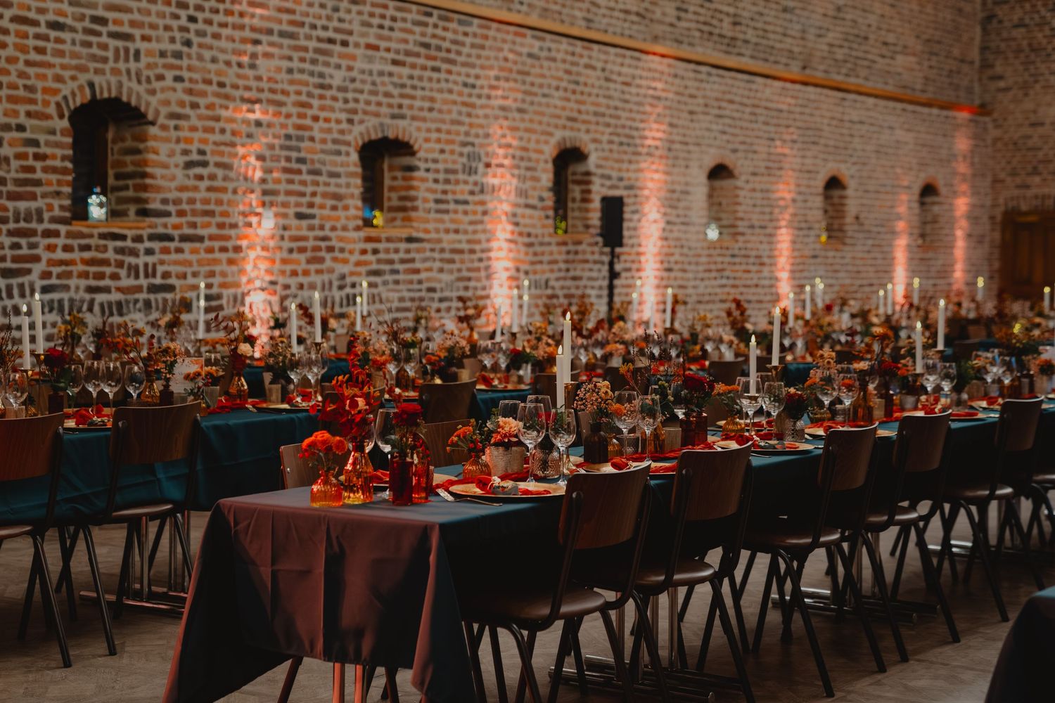 Long banquet tables with black chairs set up in industrial brick venue for wedding reception.