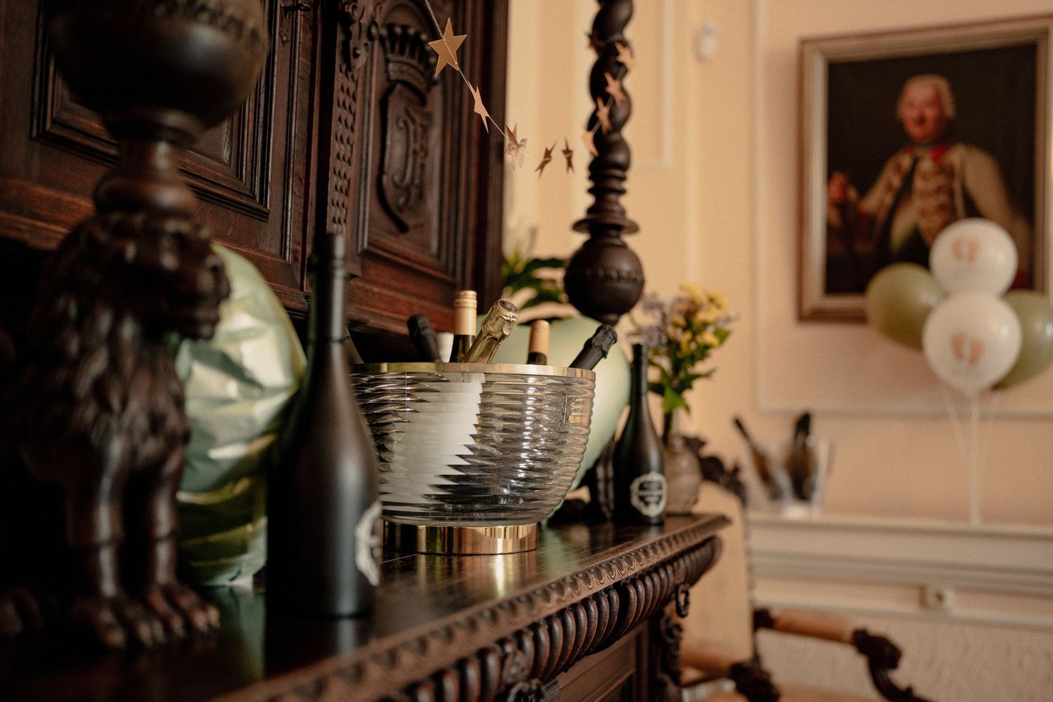 Elegant dark wood mantle with silver champagne bucket, bronze lion statue, and portrait painting in ornate interior.