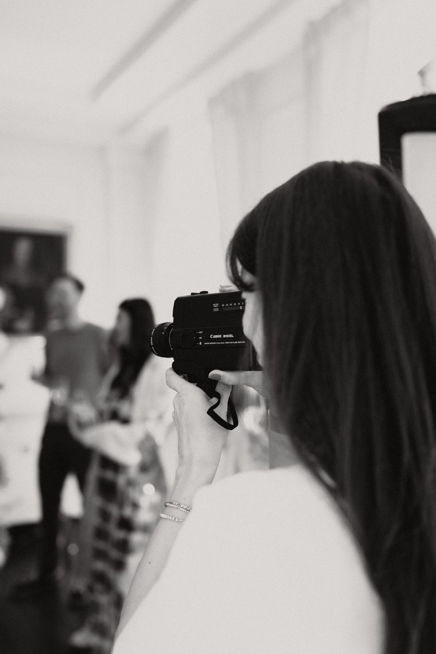 Black and white photo of a woman filming an indoor event with a Canon video camera.