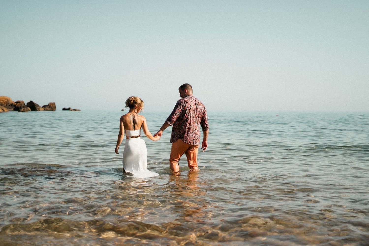Couple wades through crystal clear ocean waters during beach photography session.