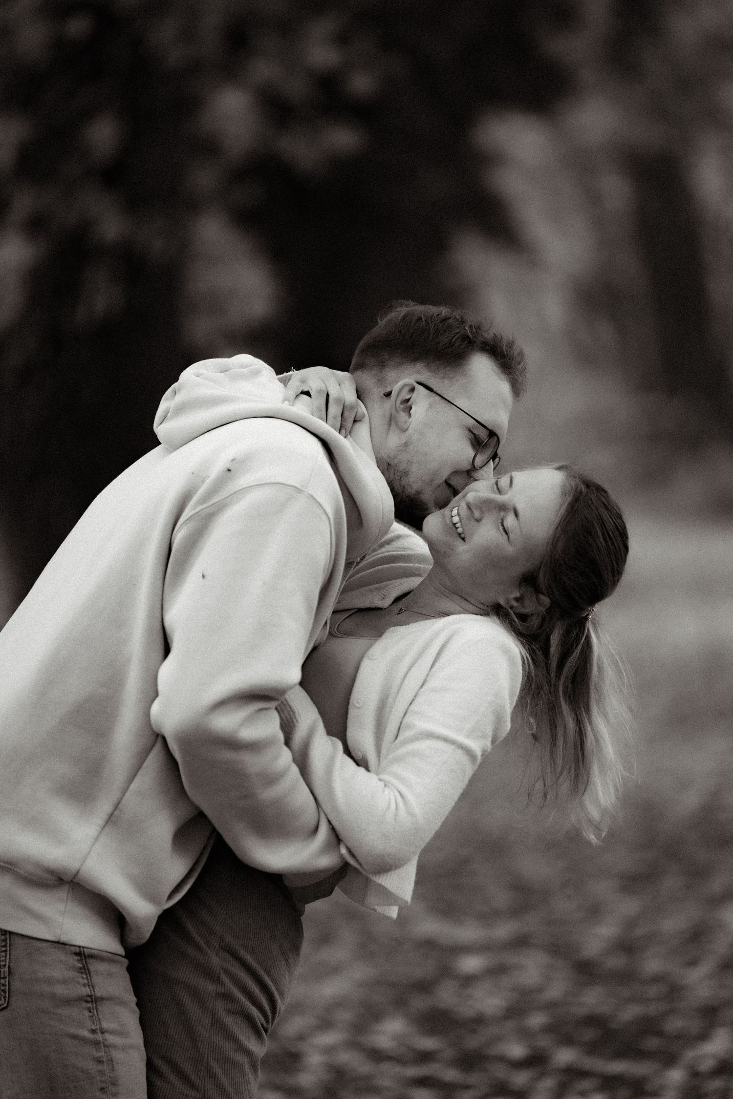 A sweet black and white portrait of a couple embracing and laughing together outdoors.