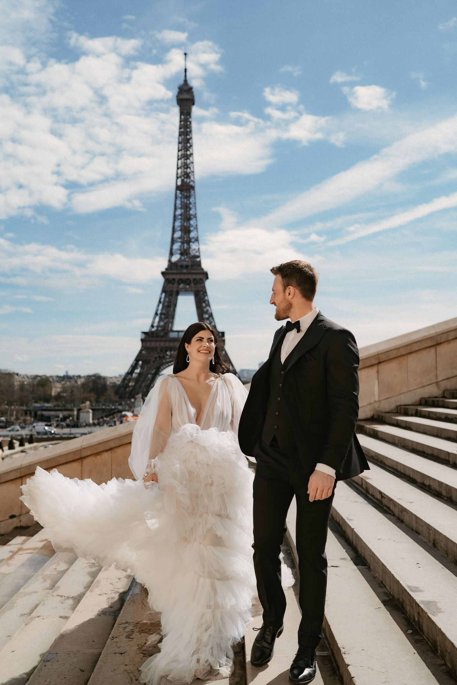 Wedding couple posing on Trocadero steps with Eiffel Tower in background on sunny day.