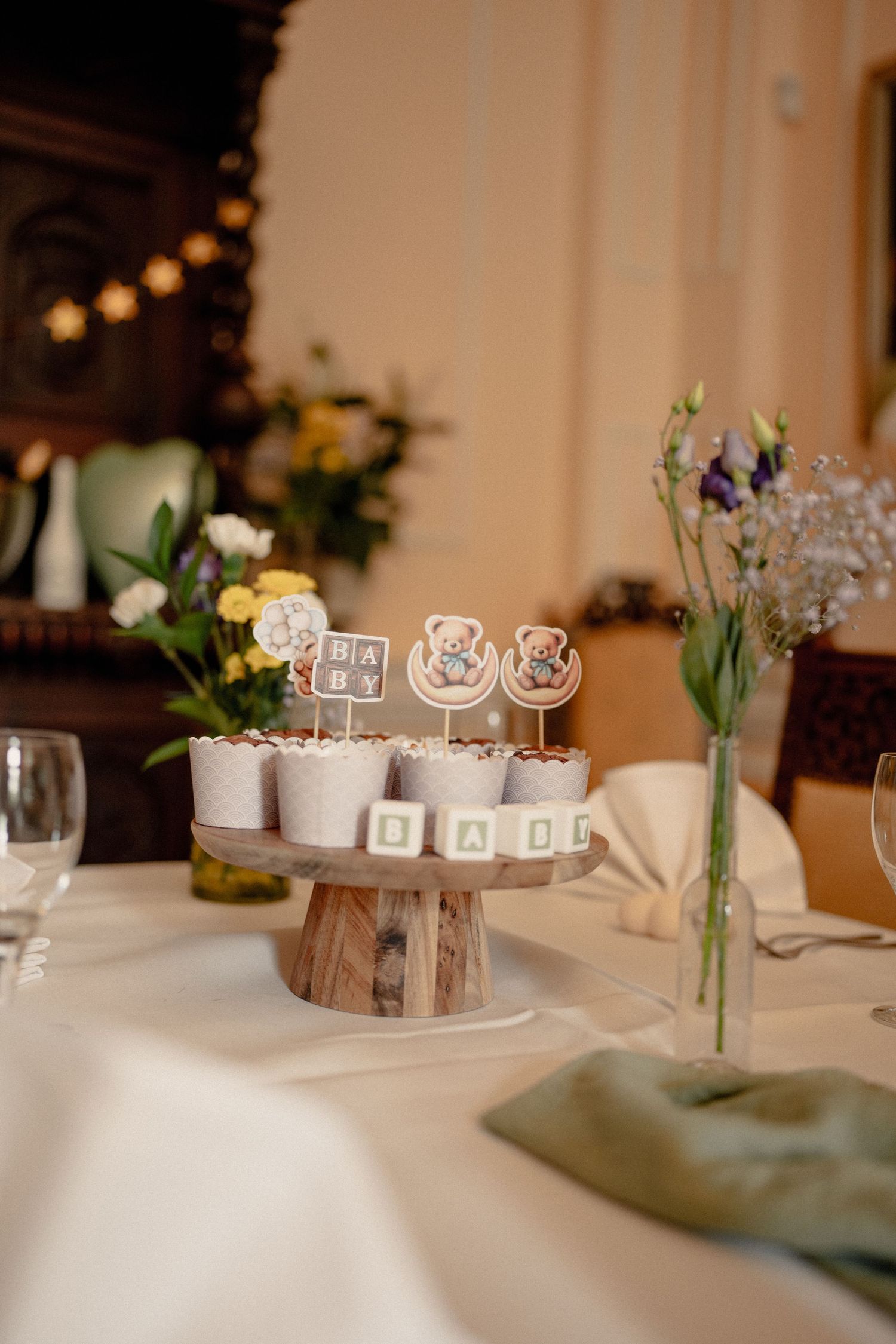 Baby shower table display with teddy bear cupcake toppers spelling BABY on a rustic wooden cake stand.