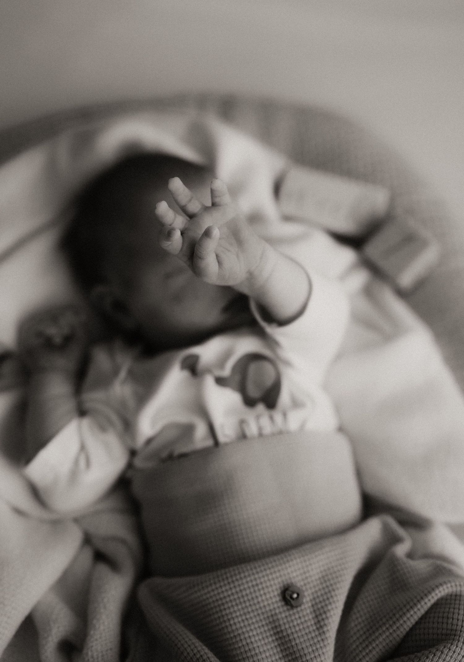 Black and white close-up photograph of a sleeping infant swaddled in soft fabric.