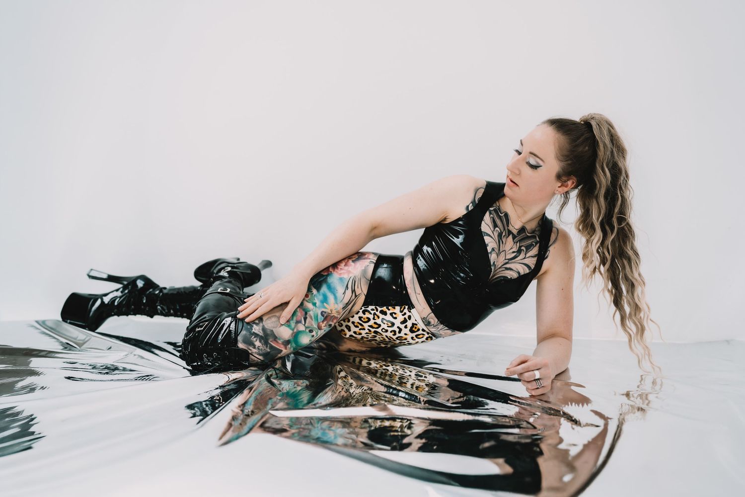 Fashion model in leopard print pants and black top poses on reflective surface with combat boots.