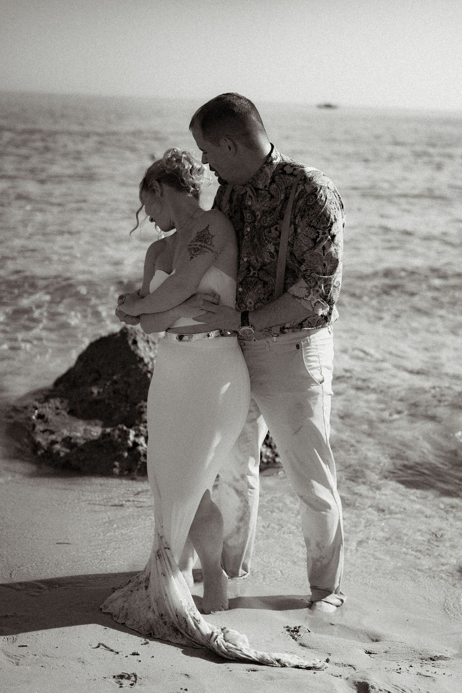 Black and white beach portrait captures tender moment between couple on sandy shore.